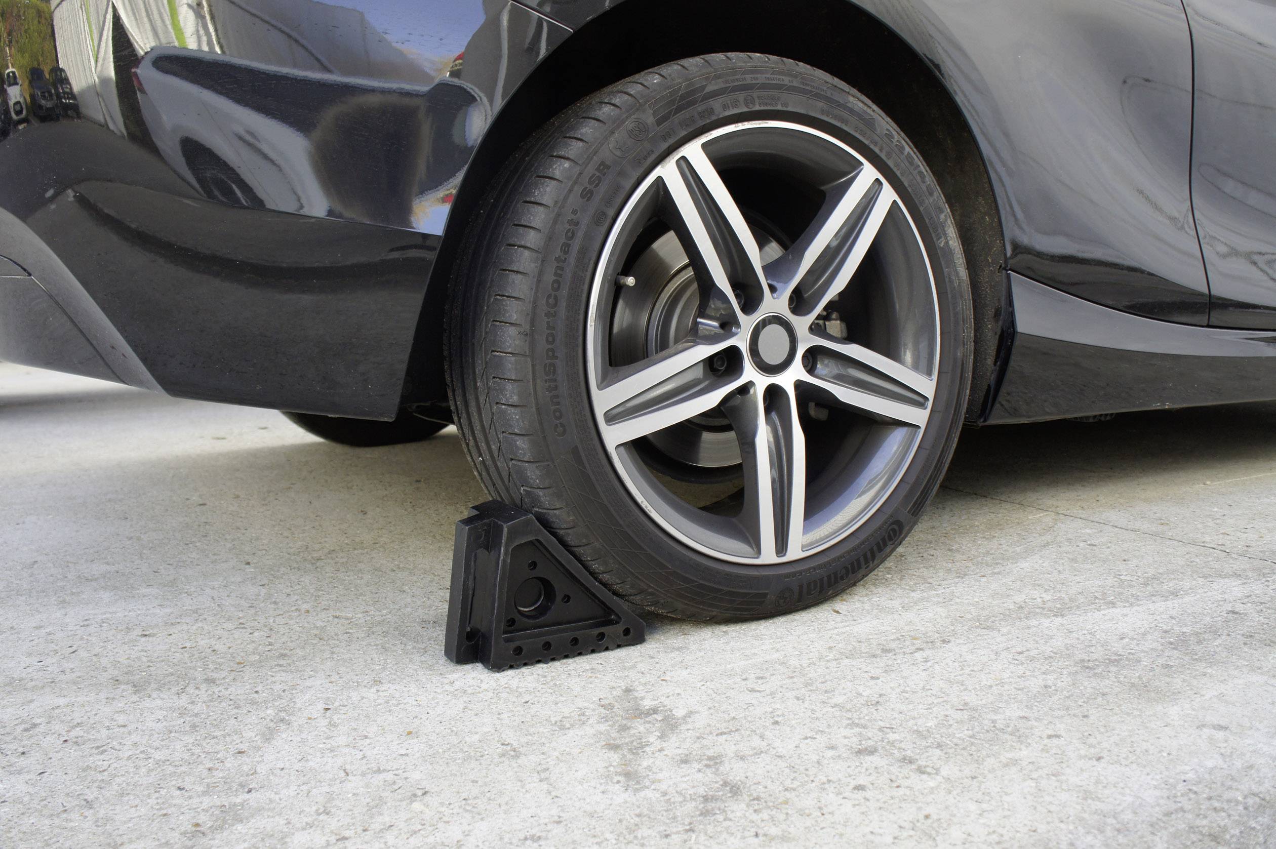 Ein schwarzes Auto mit einem Stopper vor dem Reifen, der das Fahrzeug auf einer Betonoberfläche sichert.