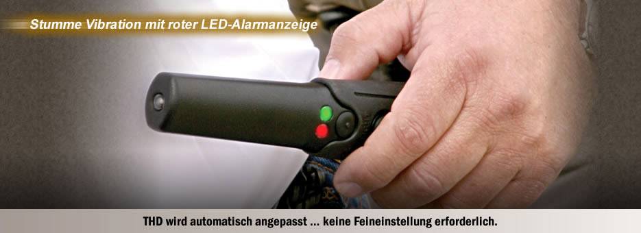 Hand hält einen schwarzen Vibrationsdetektor mit roten und grünen LED-Lichtern. Text oben: 'Stumme Vibration mit roter LED-Alarmanzeige.'