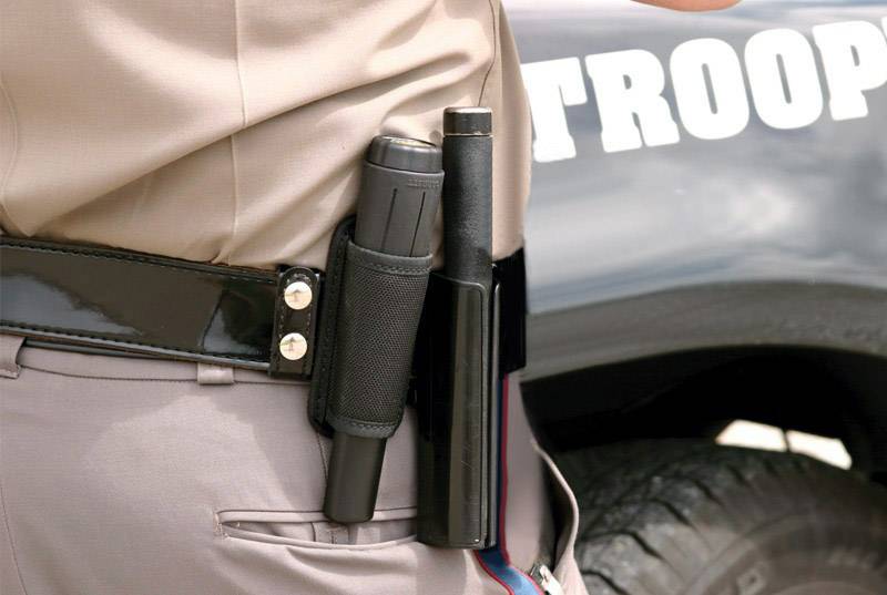 Ein Polizist steht neben einem Einsatzfahrzeug. Der Fokus liegt auf dem Schlagstock und der Taschenlampe in der Dienstgürtelhalterung.