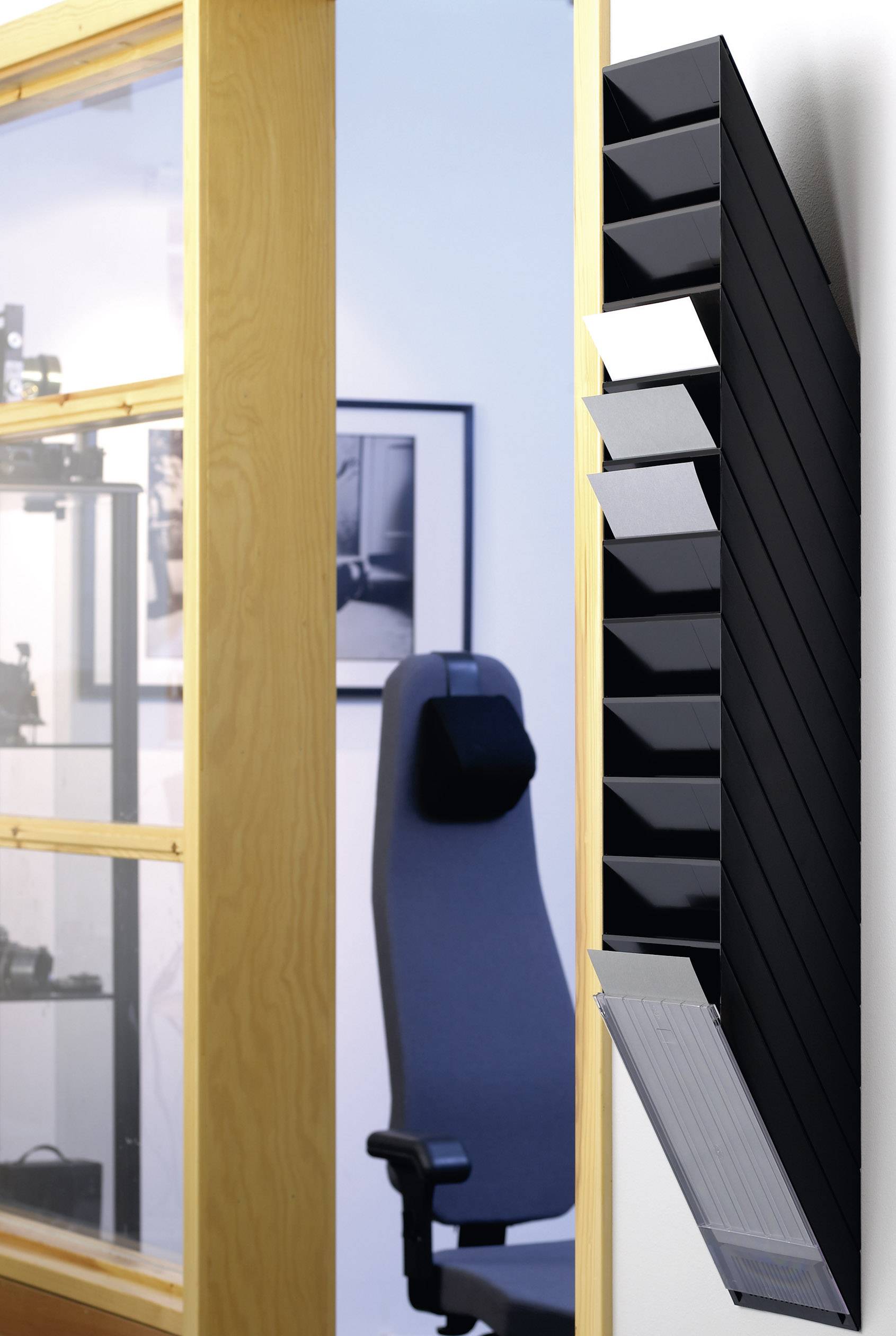 Ein schwarzes Fachregelbrett an einer weißen Wand enthält leere Schilder. Im Hintergrund sind ein Stuhl und ein Schrank mit Glasfront sichtbar.