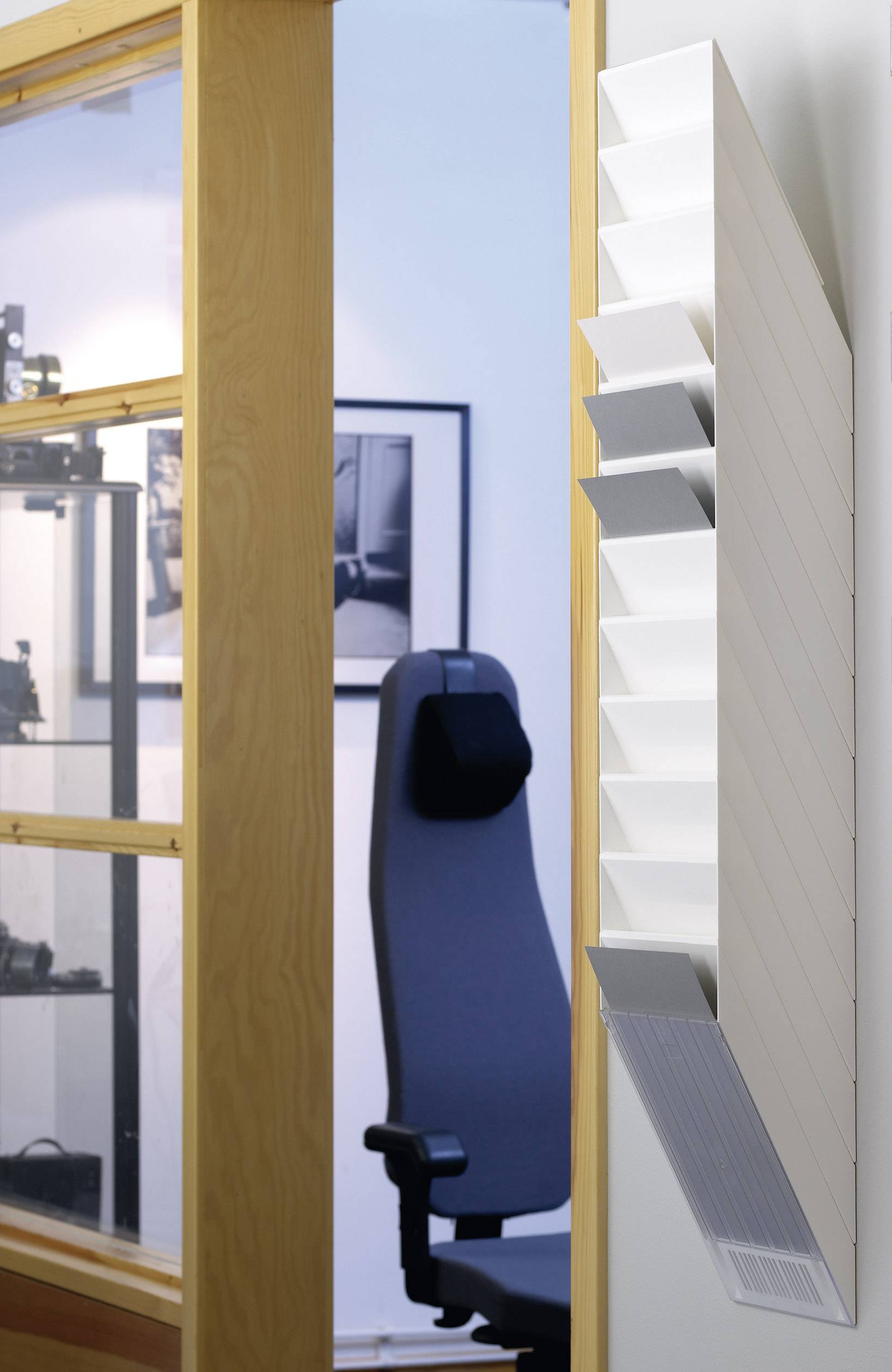 Ein moderner Büroraum mit einem schwarzen Bürostuhl vor einer Glaswand. An der Wand hängt ein Heizkörper mit weißen Lamellen.