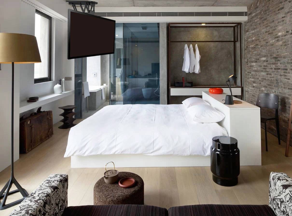 Modernes Hotelzimmer mit einem zentralen Doppelbett, Flachbildfernseher an der Wand, und einer offenen Badezimmerwand.