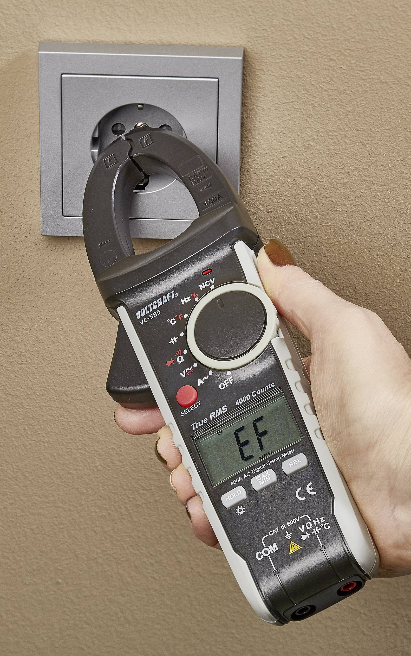 Eine Hand hält ein Multimeter, das eine Steckdose misst. Das Display zeigt 'EF' an.