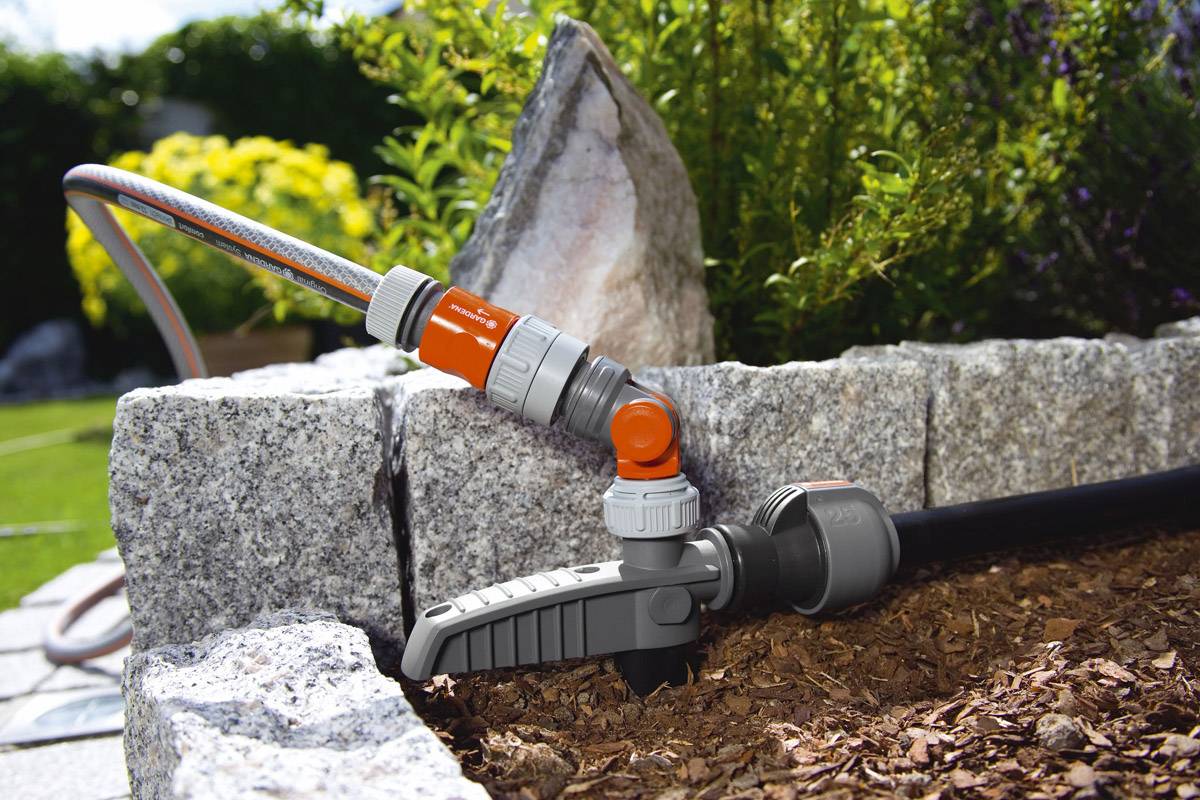 Ein Gartenschlauch ist an eine Wasserpumpe angeschlossen, die in einem Garten neben Steinplatten und Mulch installiert ist.