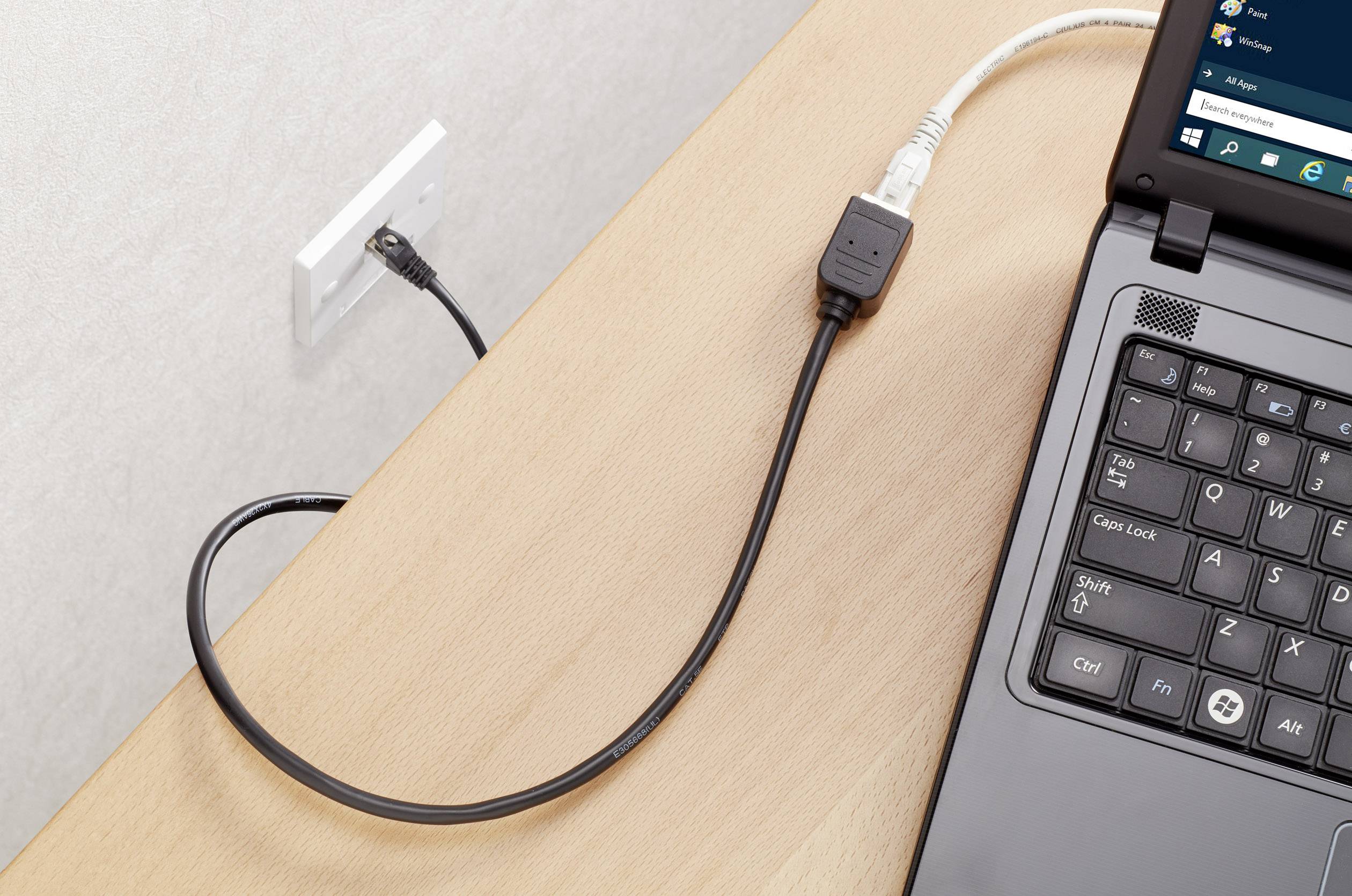 Ein Laptop ist per Ethernet-Kabel mit einer Wandsteckdose verbunden. Der Bildschirm zeigt ein Betriebssystem-Fenster.