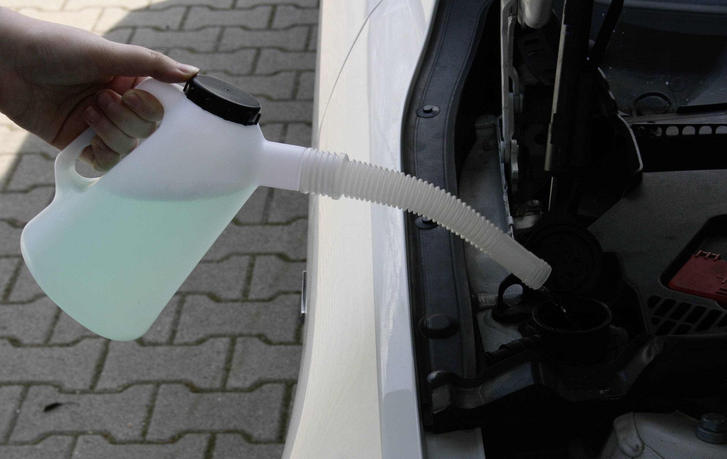 Eine Hand füllt mit einer Flasche blauer Flüssigkeit Scheibenwaschmittel in den Behälter eines Autos ein.