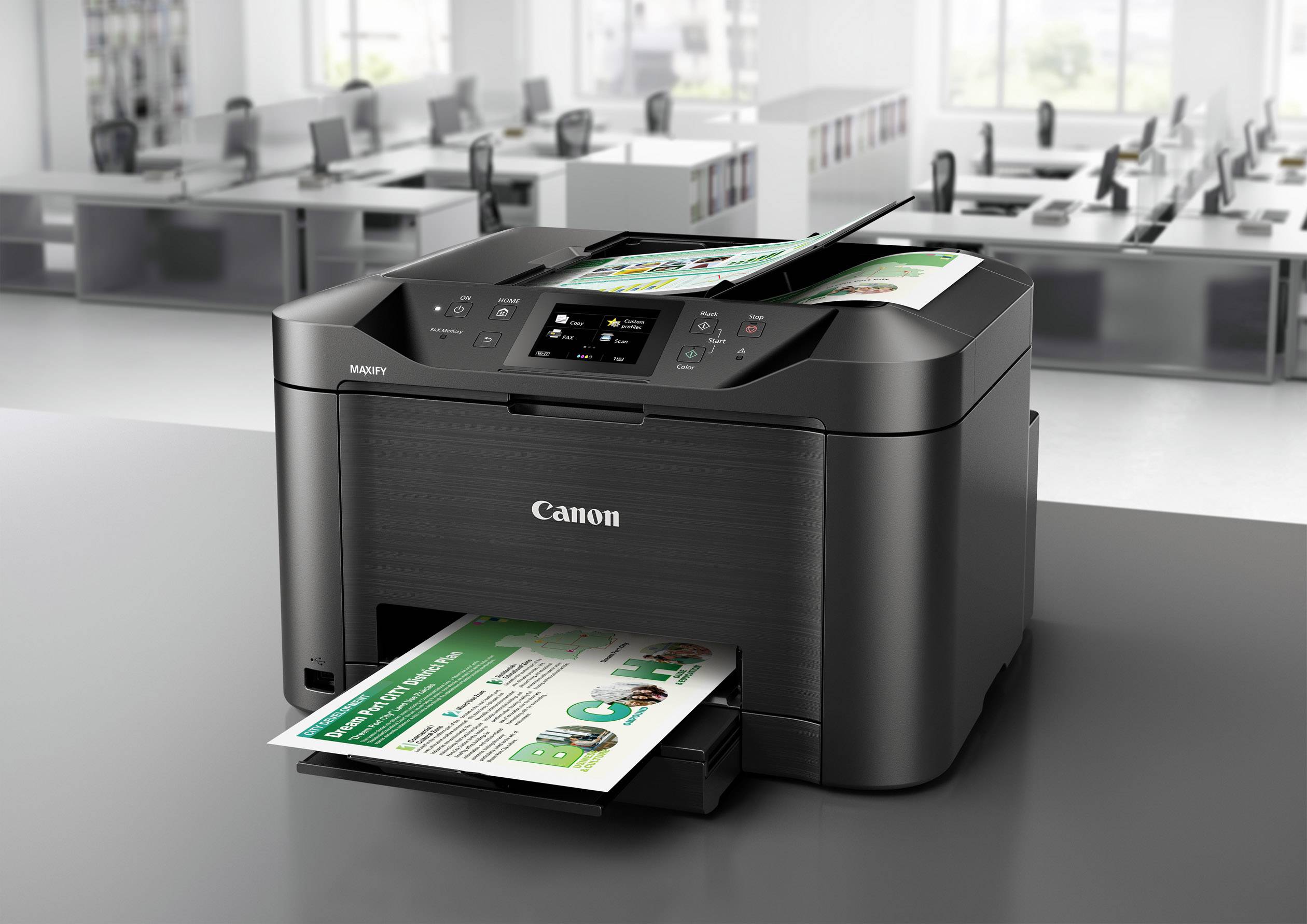 Schwarzer Drucker auf Tisch in modernem Büro, druckt farbiges Dokument. Im Hintergrund leere Arbeitsplätze mit Computern.