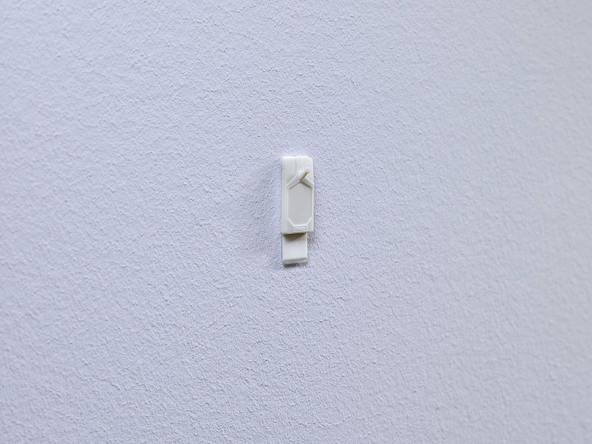 Ein weißer Haken, montiert auf einer strukturierten weißen Wand, vorgesehen zum Aufhängen kleinerer Objekte.