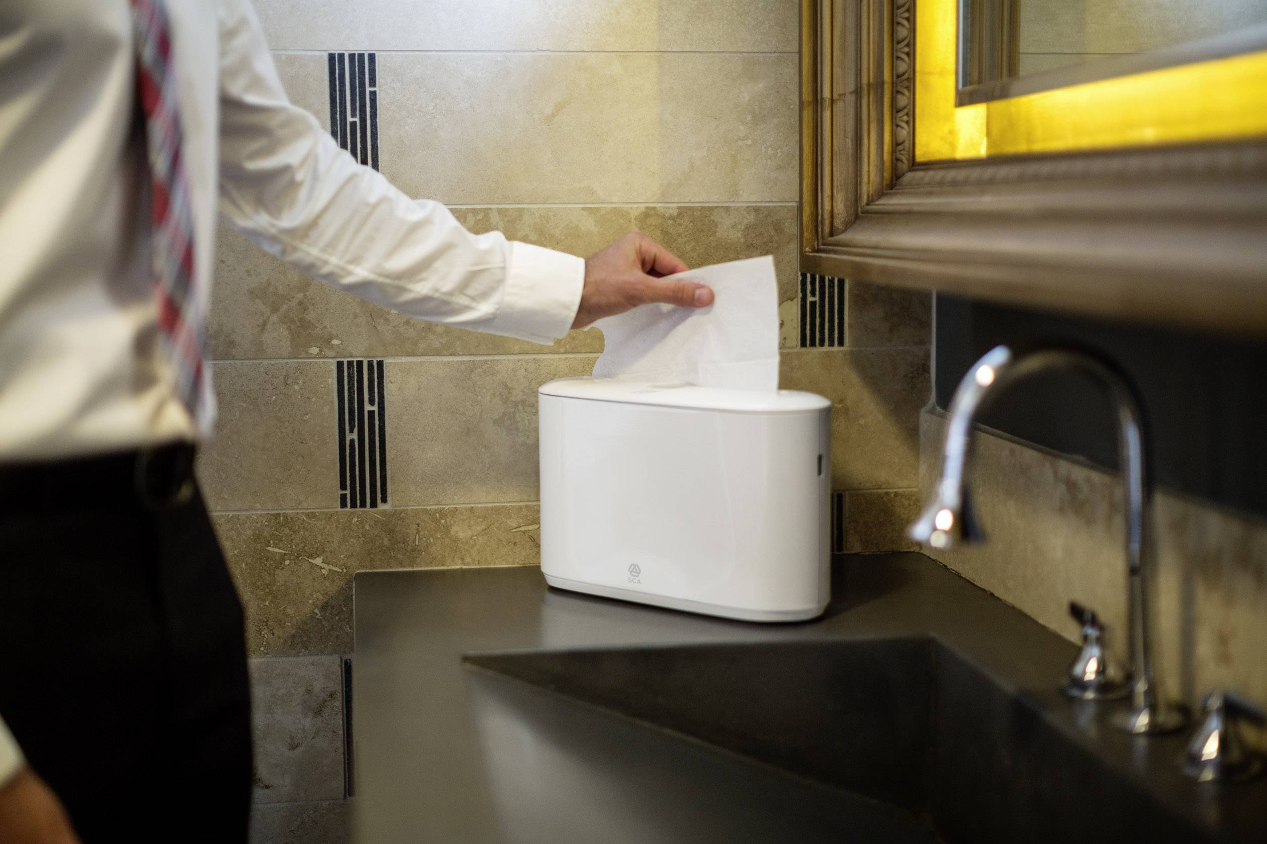Ein Mensch im Anzug steckt ein Papierhandtuch in einen modernen Papierhandtuchspender in einem stilvoll eingerichteten Badezimmer.