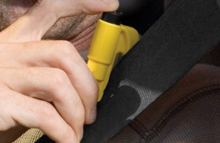 Person hält einen gelben Sicherheitsgurt-Schneider und schneidet damit den Sicherheitsgurt in einem Auto durch.