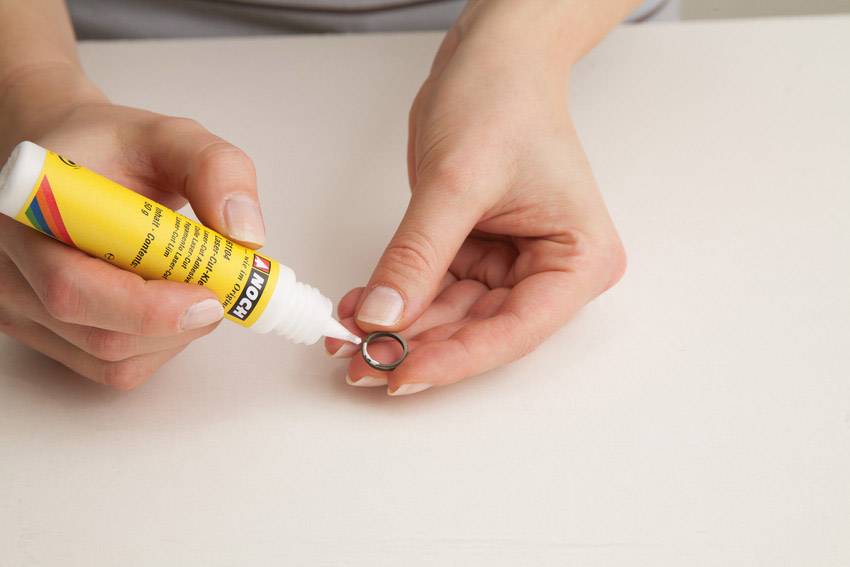 Eine Person trägt Klebstoff aus einer gelben Tube auf einen kleinen Metallring auf.