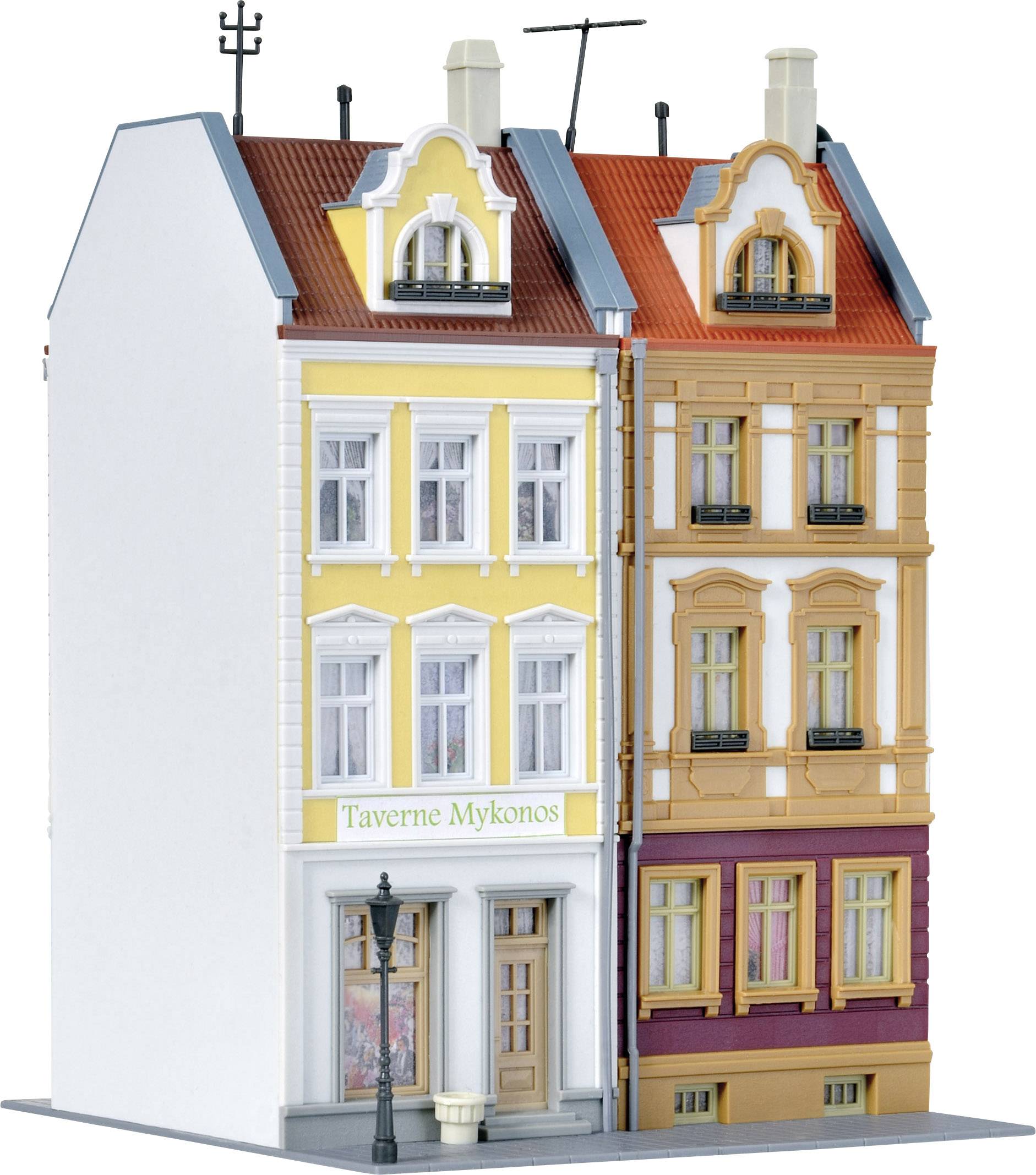 Zwei nebeneinander stehende Modellhäuser mit verzierten Fassaden. Eines hat ein gelbes, das andere ein sandfarbenes Äußeres. Zwischen ihnen steht ein Schild mit der Aufschrift 'Taverne Mykonos'.