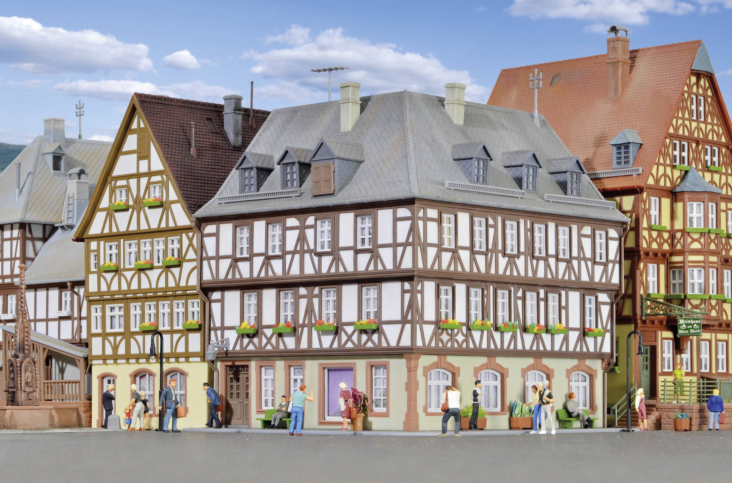 Fachwerkhäuser in einer historischen Altstadt mit mehreren Menschen, die die Straße entlang spazieren. Blauer Himmel im Hintergrund.