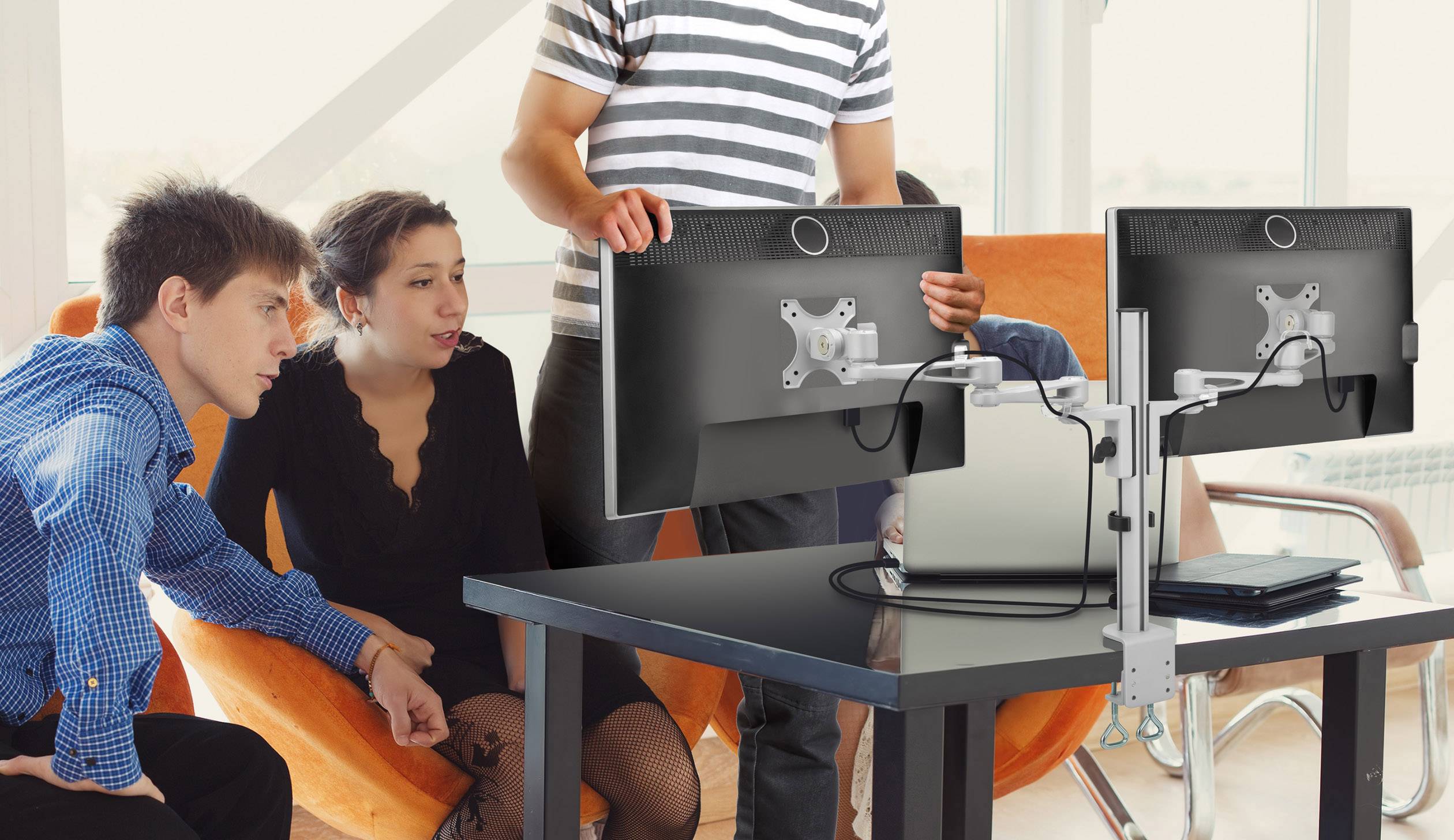 Vier Personen sitzen um einen Tisch mit zwei Monitoren. Eine Person steht und zeigt auf einen Bildschirm. Sie scheinen zu diskutieren.
