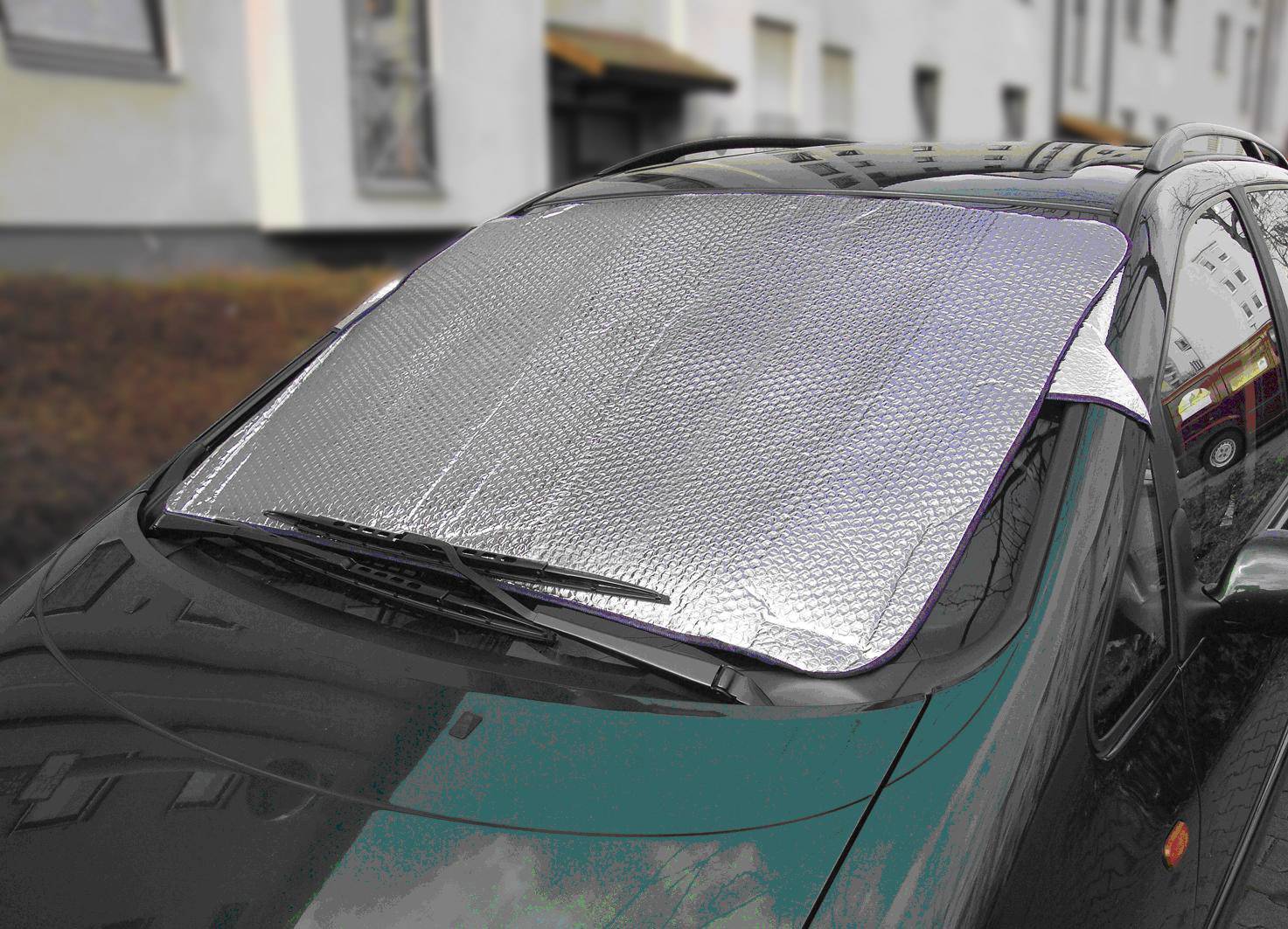Auto mit silberner Sonnenschutzabdeckung auf der Frontscheibe, geparkt an der Straße vor einem Gebäude.