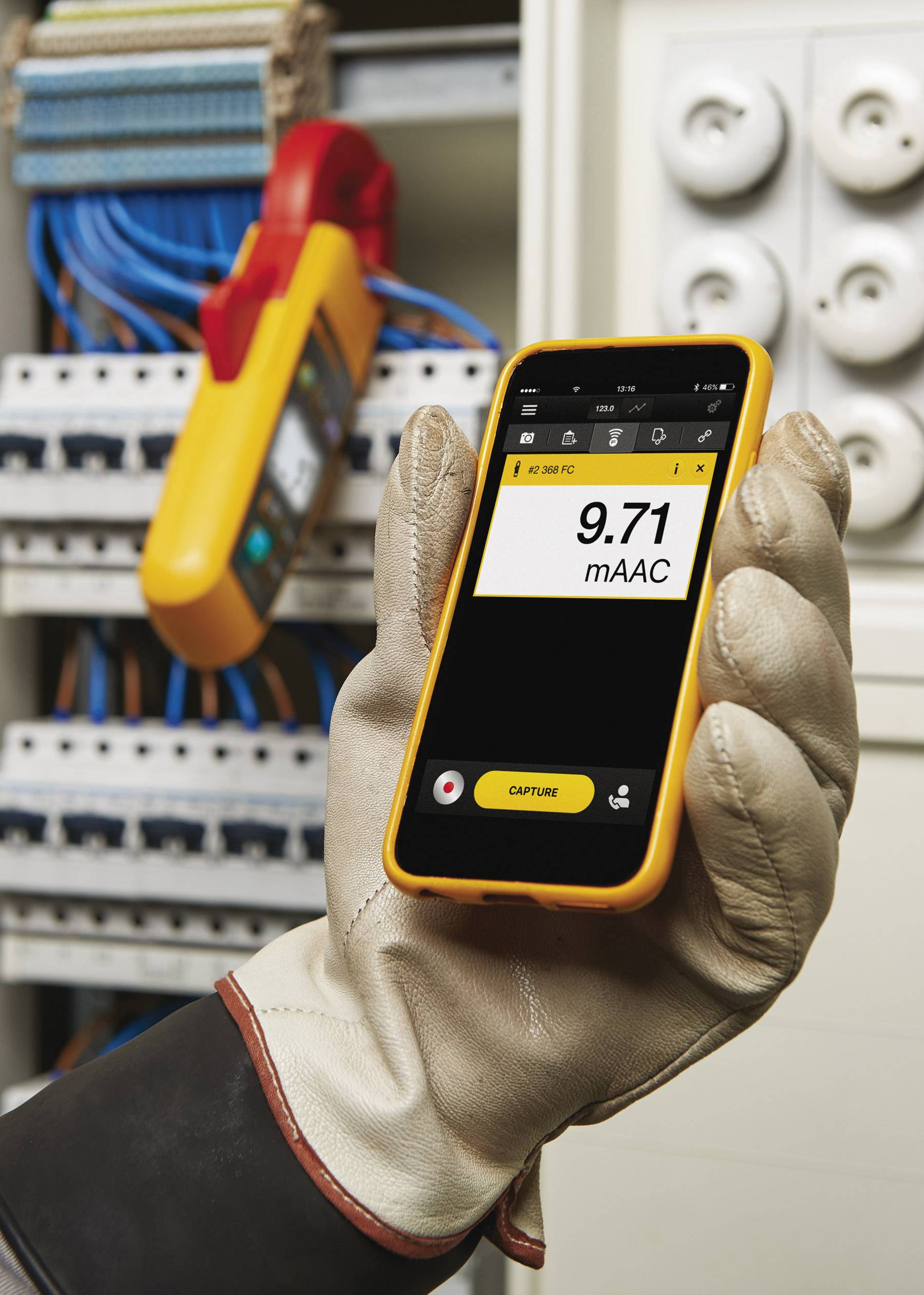 Eine Person mit Handschuhen hält ein Multimeter, das 9,71 mAAC anzeigt, vor einem Sicherungskasten mit offenen Abdeckungen.