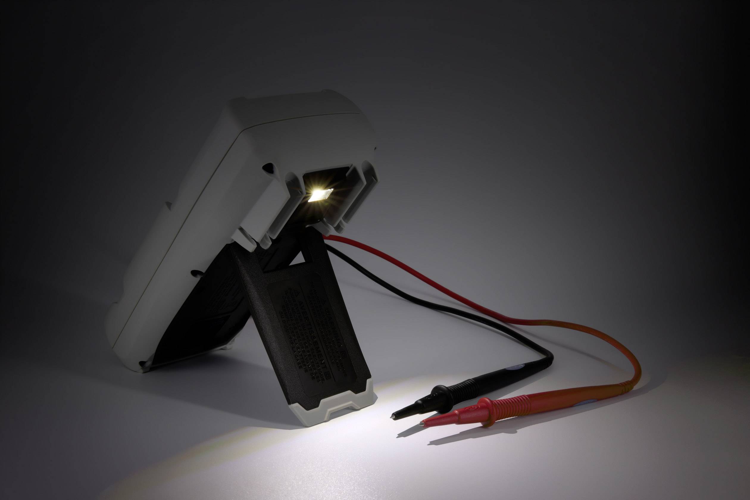 Multimeter mit beleuchtetem Display und zwei angeschlossenen Prüfspitzen liegt schräg auf einer Oberfläche, zeigt Messbereitschaft.