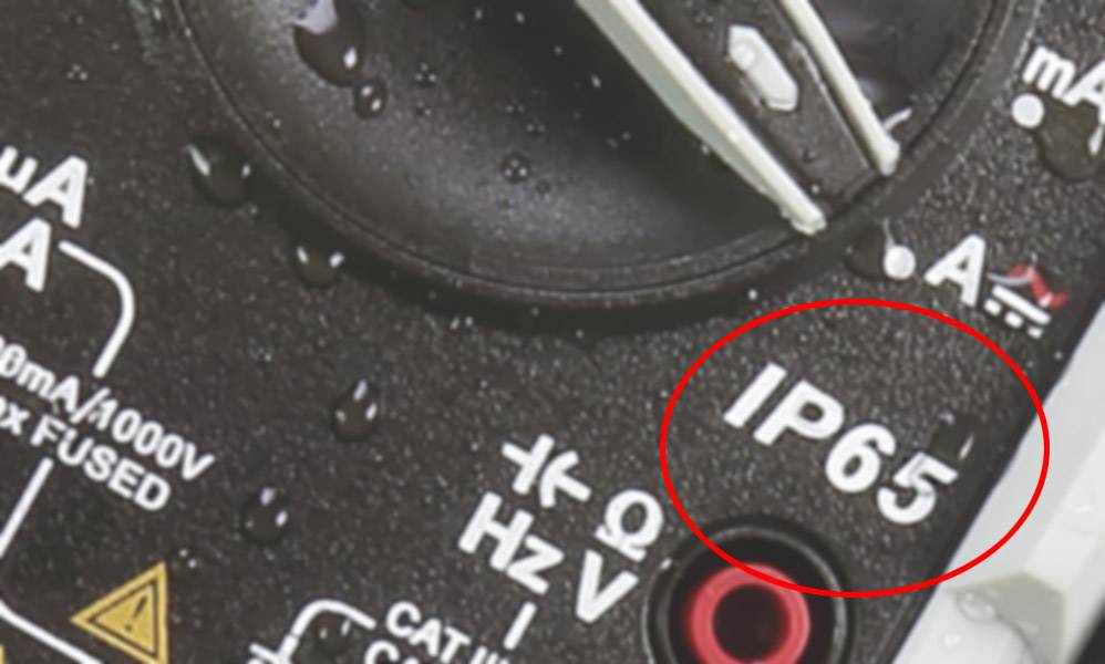 Multimeter mit IP65-Schutzkennzeichnung, umgeben von Wassertropfen, zeigt Wasserdichtigkeit an.