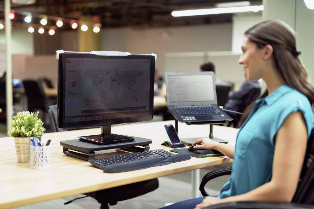 Eine Frau arbeitet an einem Schreibtisch mit zwei Bildschirmen. Auf dem großen Bildschirm ist eine Weltkarte zu sehen.