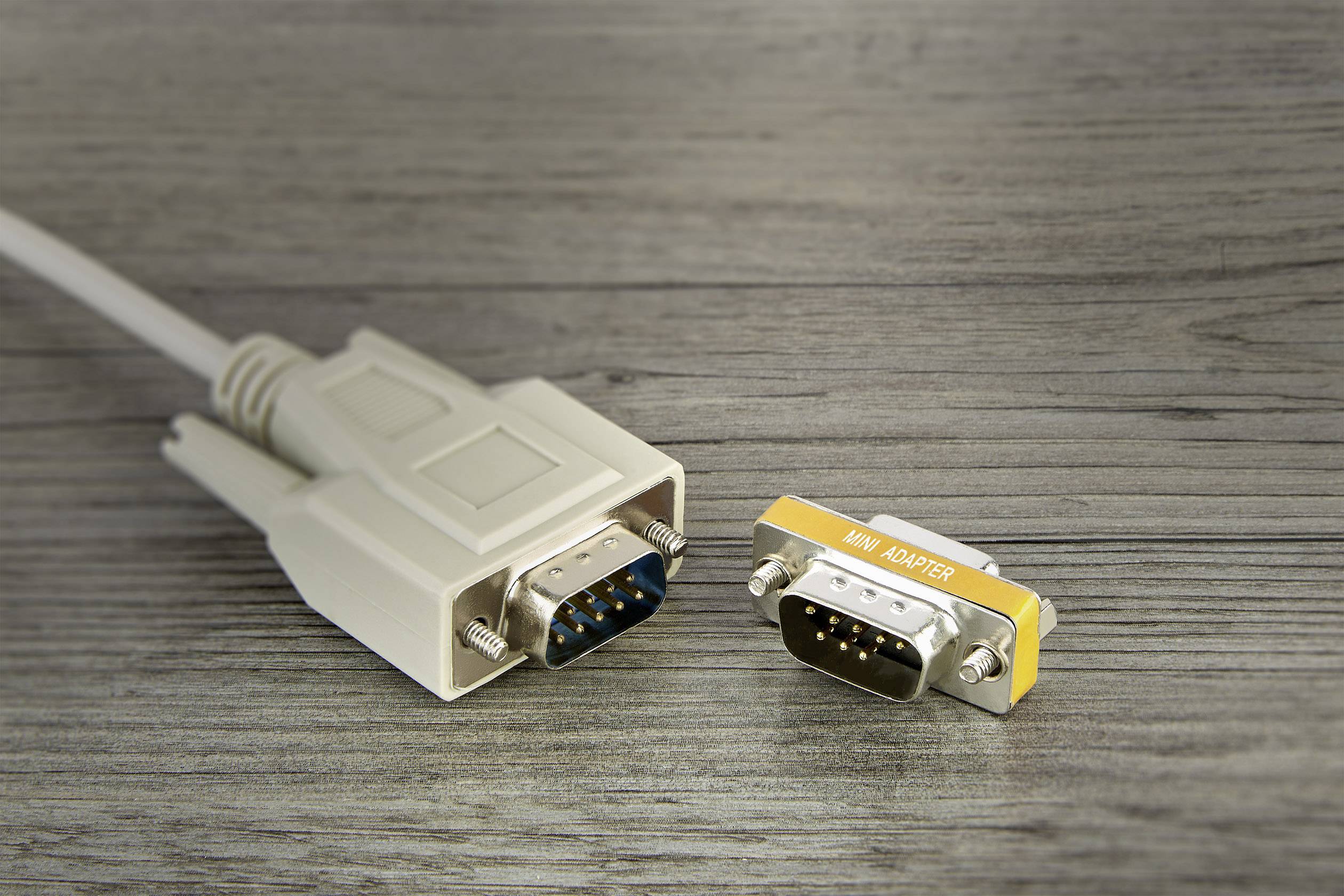 VGA-Kabel mit 9-poligem Stecker neben einem 9-poligen Mini-Adapter auf einem Holztisch