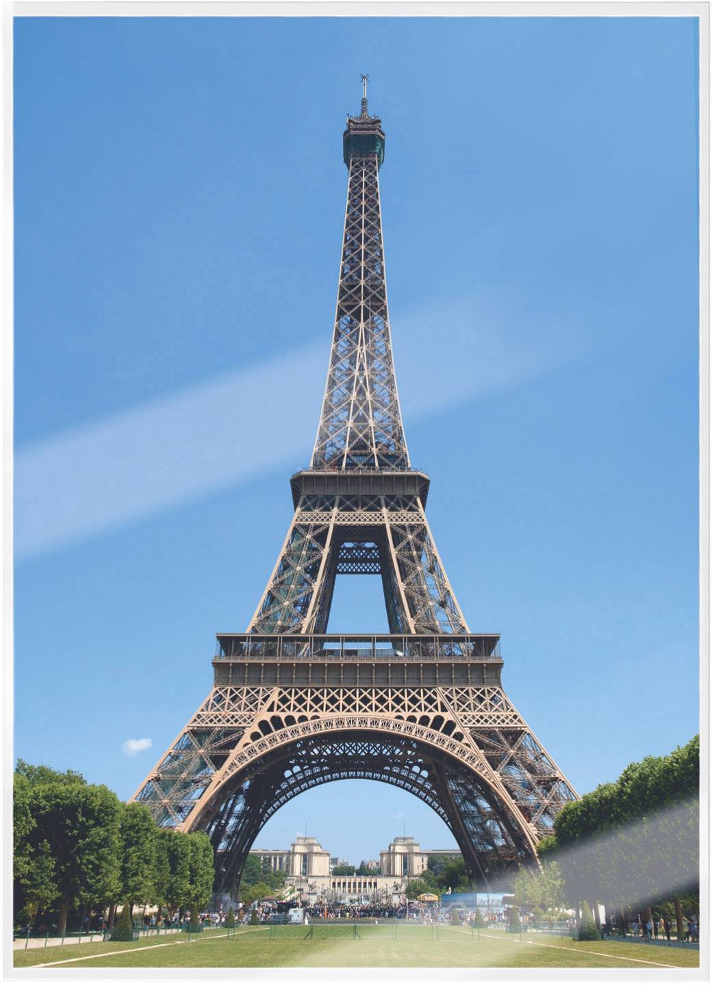 Der Eiffelturm in Paris bei klarem Himmel, mit grünen Bäumen im Vordergrund und dem Champ de Mars.