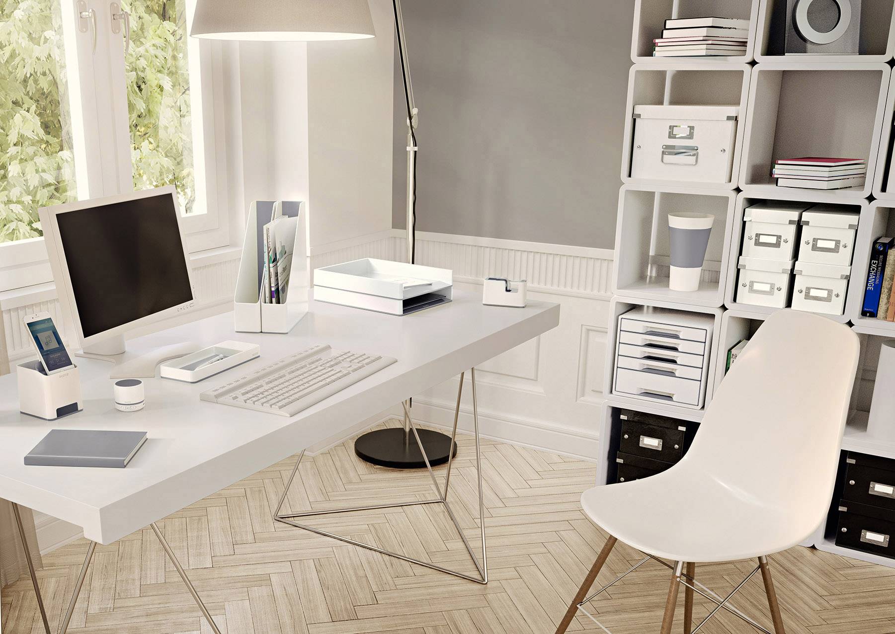 Moderner, gut organisierter Arbeitsplatz mit Schreibtisch, Monitor, Tastatur, Laptop und Regalen voller Ordner und Boxen neben einem Fenster.