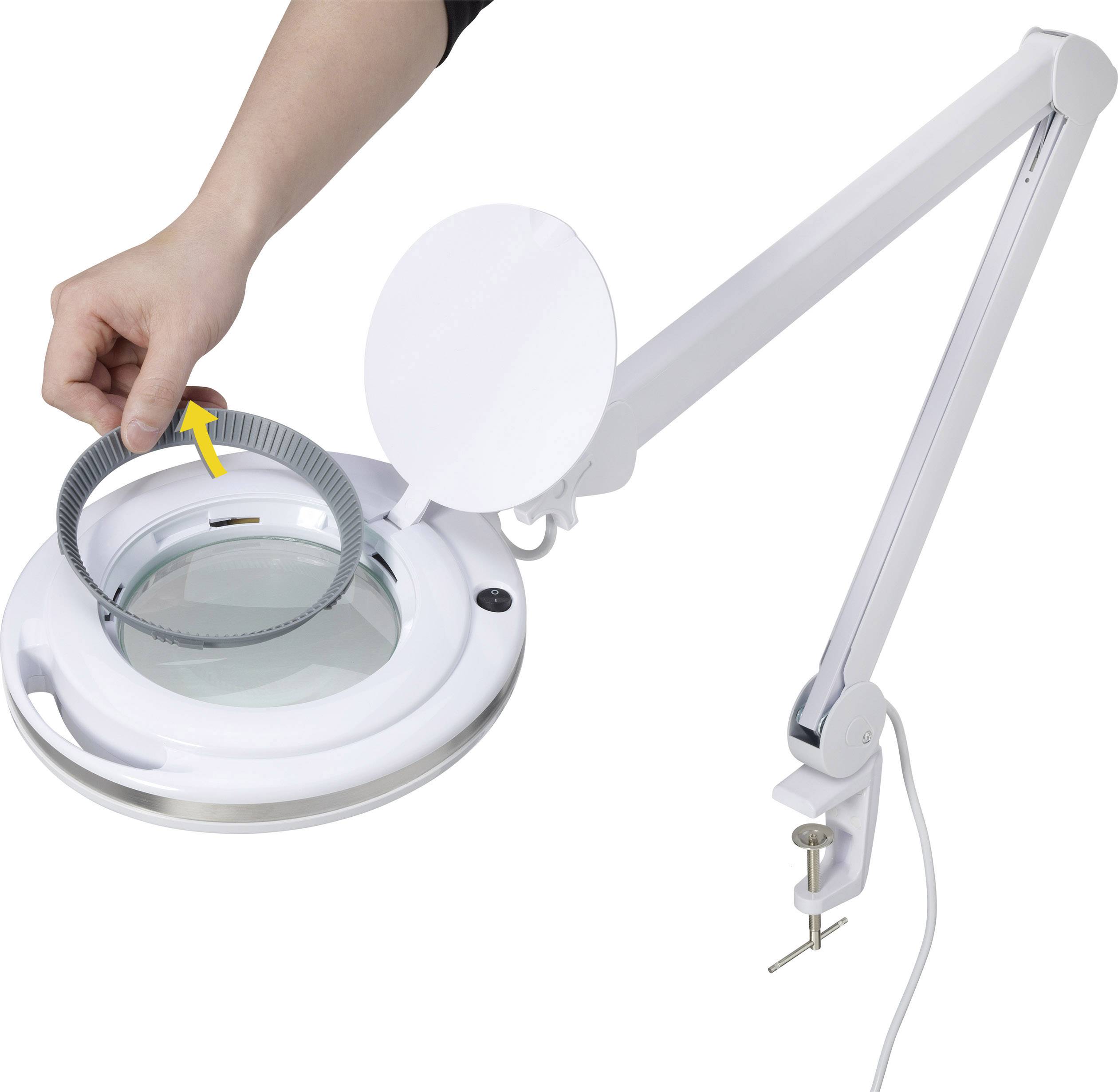 Eine Hand befestigt ein rundes Bauteil an einer Lupenlampe mit verstellbarem Arm, die an einem Tisch montiert ist.