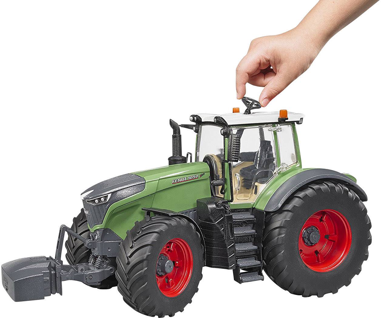 Ein Modelltraktor mit grüner Karosserie und roten Reifen. Eine Hand dreht das Lenkrad oben am Traktor.