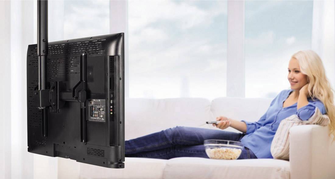 Eine Frau sitzt entspannt auf einem Sofa und schaut auf einen an der Decke montierten Fernseher. Neben ihr steht eine Schale Popcorn.