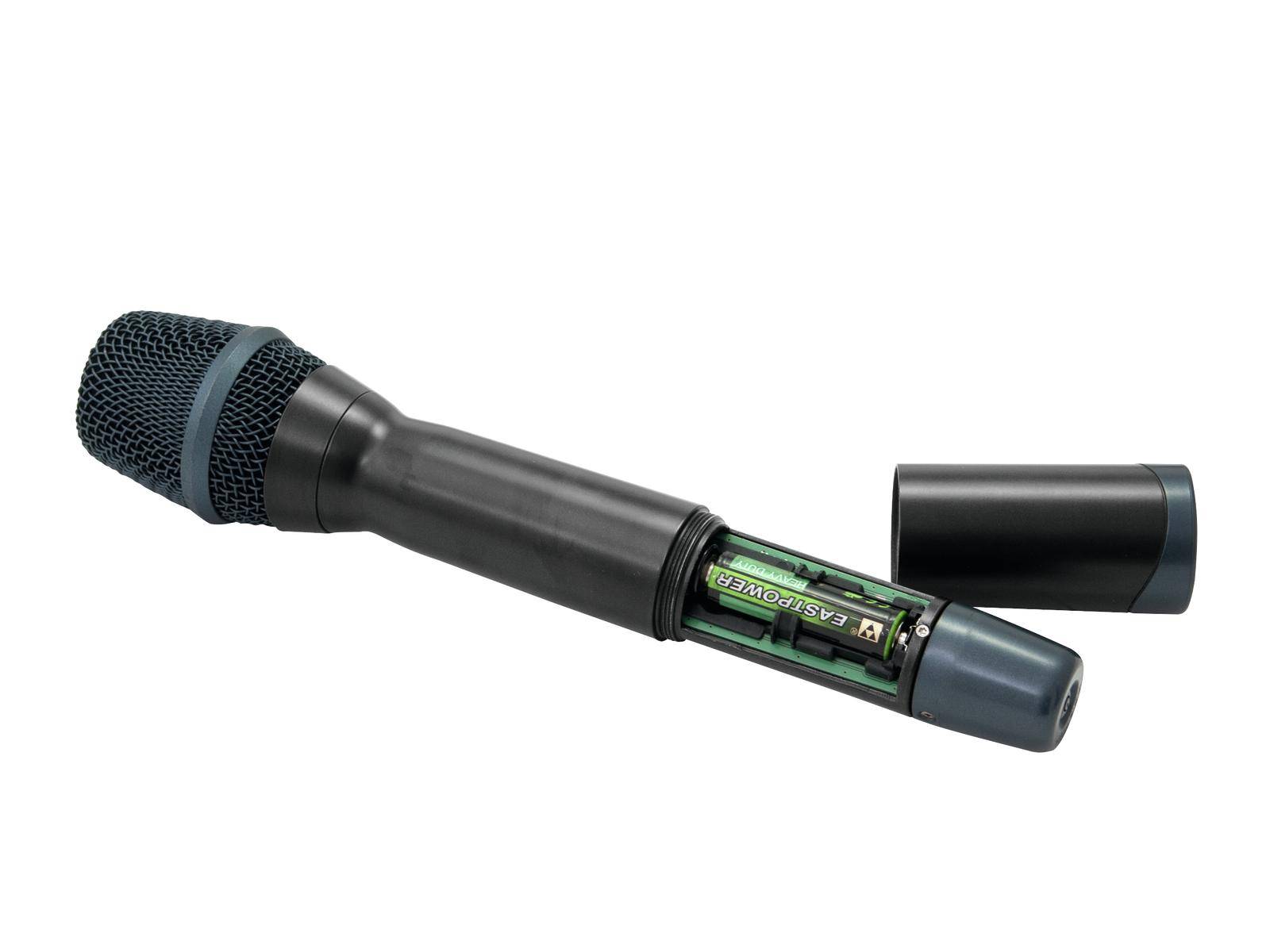 Ein schwarzes schnurloses Mikrofon liegt geöffnet, zeigt den Batteriefachbereich mit zwei grünen AA-Batterien, Deckel daneben.
