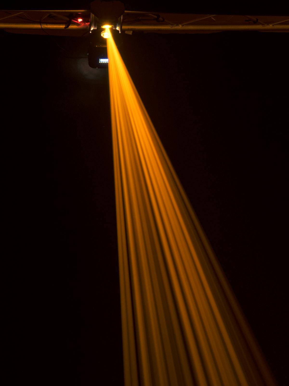 Ein einzelner gelber Lichtstrahl strahlt von oben abwärts in einem dunklen Raum, erzeugt eine eindrucksvolle Licht-Schatten-Wirkung.