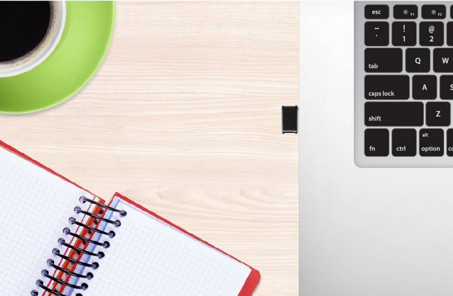 Auf einem Holztisch liegen ein aufgeschlagenes, kariertes Notizbuch und eine Tasse Kaffee. Rechts oben ist ein Teil einer Laptop-Tastatur zu sehen.