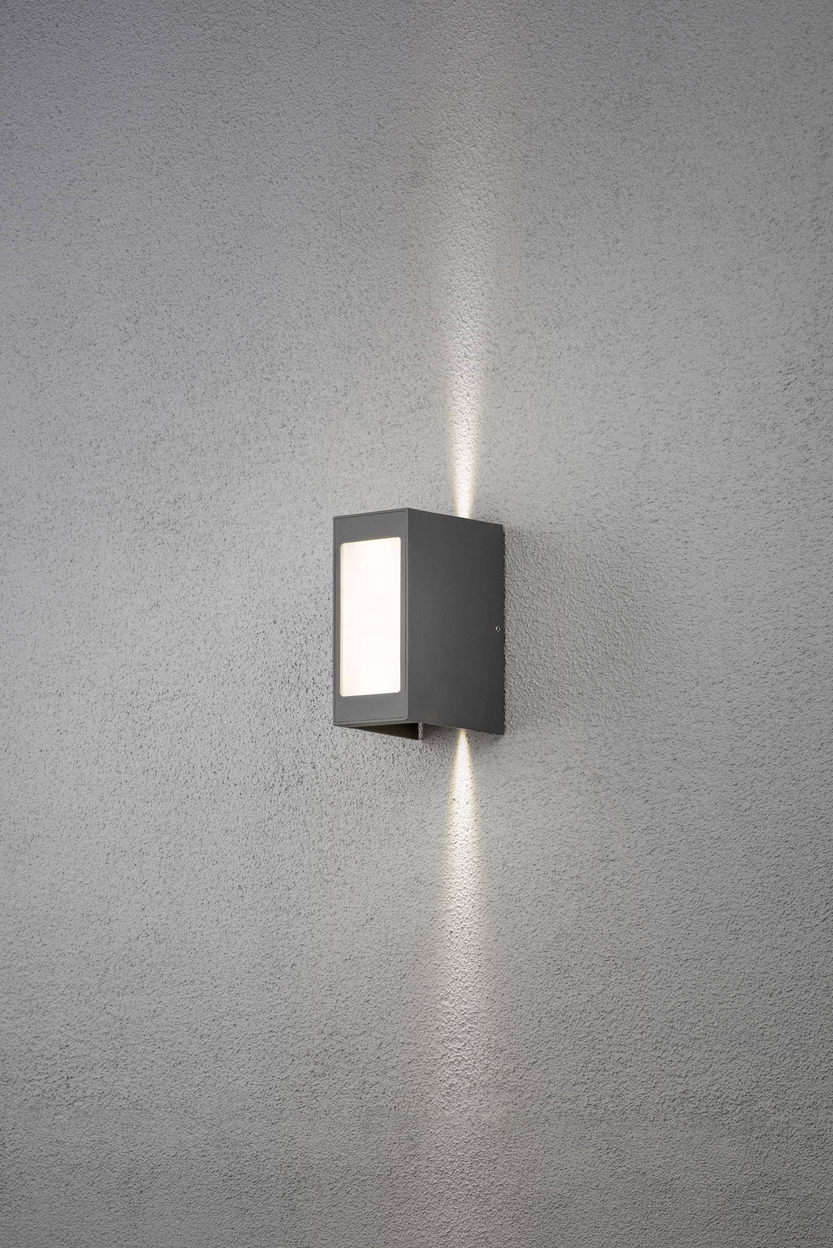 Wandleuchte mit rechteckigem Schirm, die sowohl nach oben als auch nach unten auf eine graue Wand Licht strahlt.