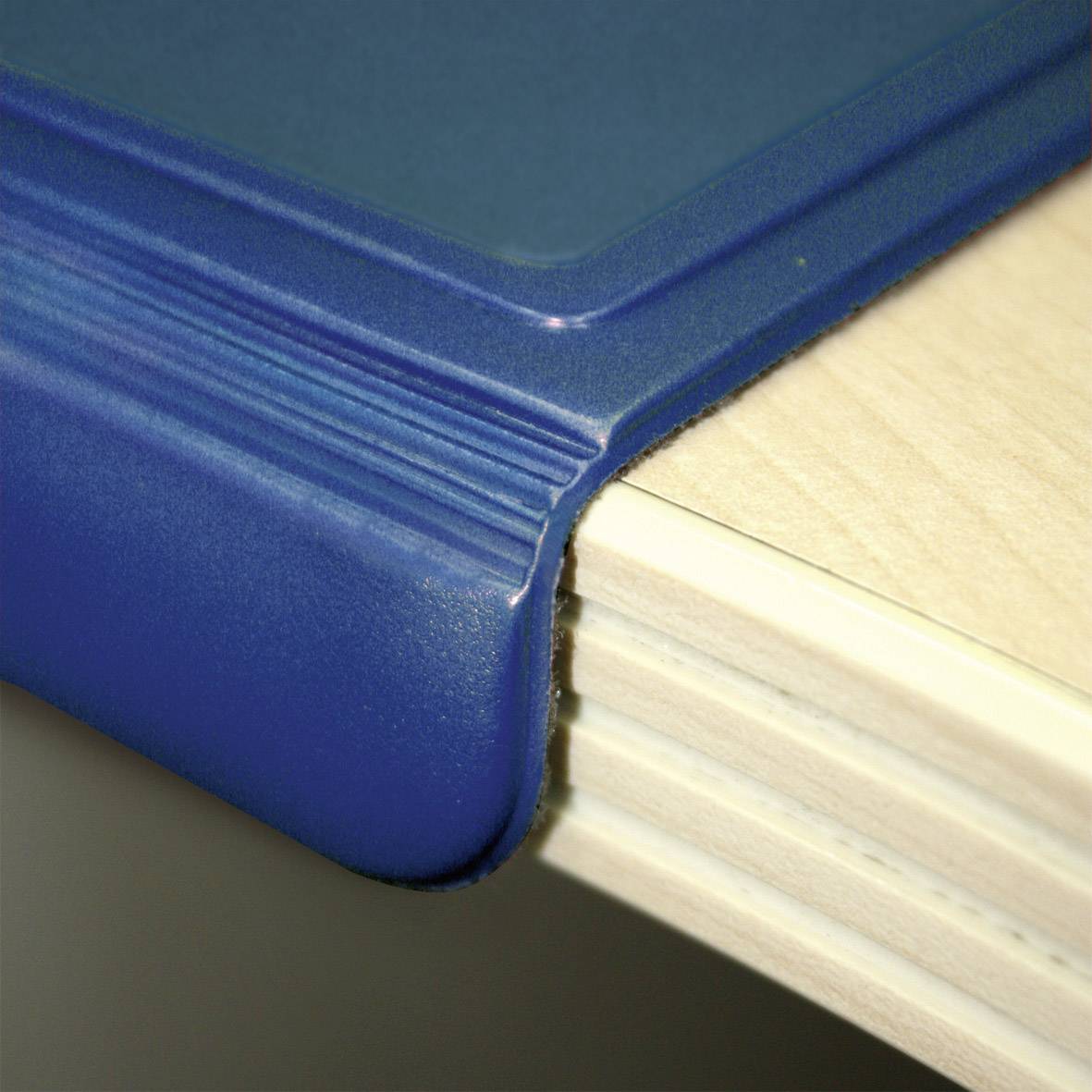 Blauer Kantenschutz auf einem Tischrand zum Schutz vor Verletzungen und Abnutzung.