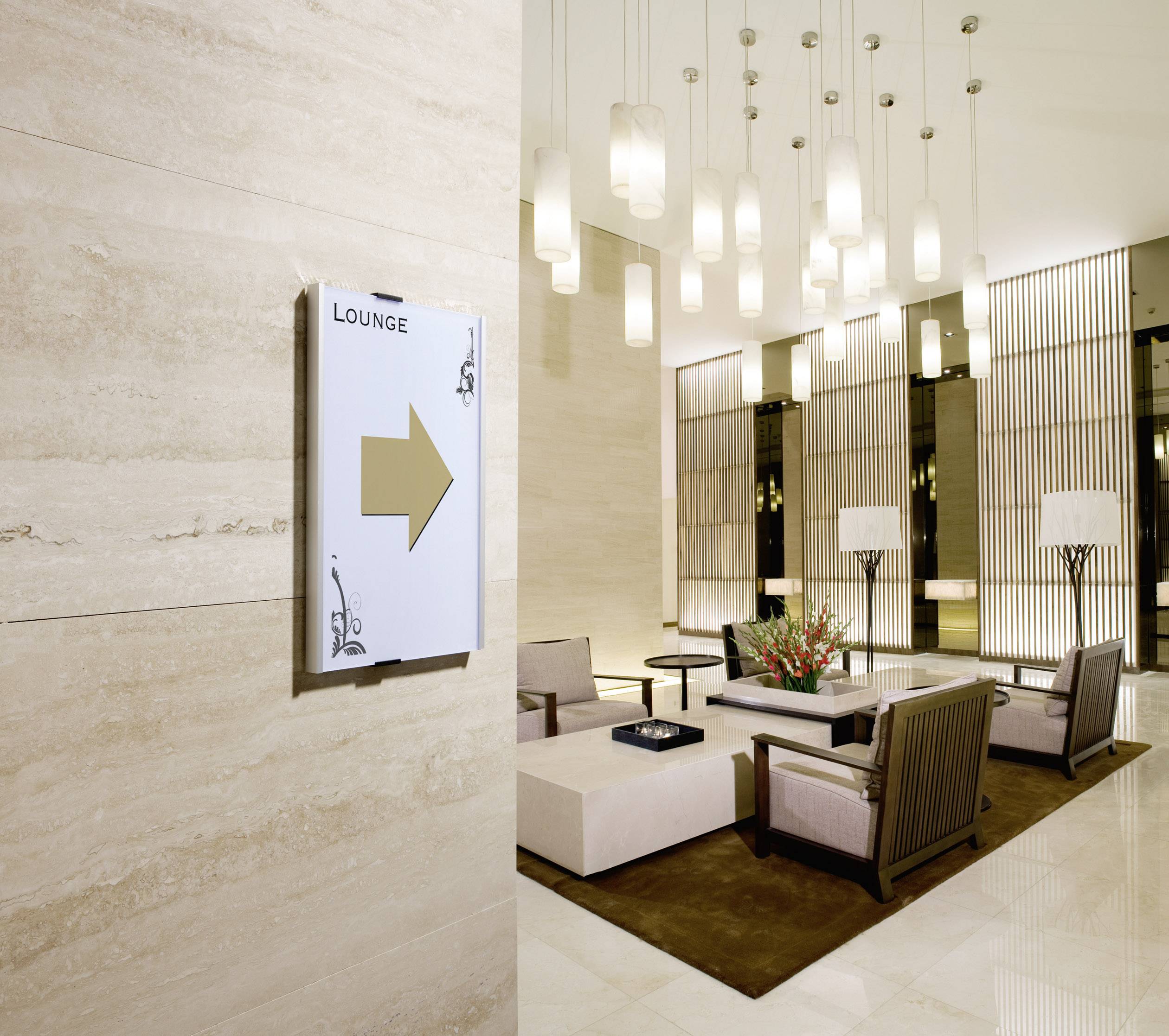 Eine elegante Hotel-Lounge mit modernen Möbeln, dezenten Beleuchtungselementen und einem Wegweiser zur 'Lounge' mit einem Pfeil.