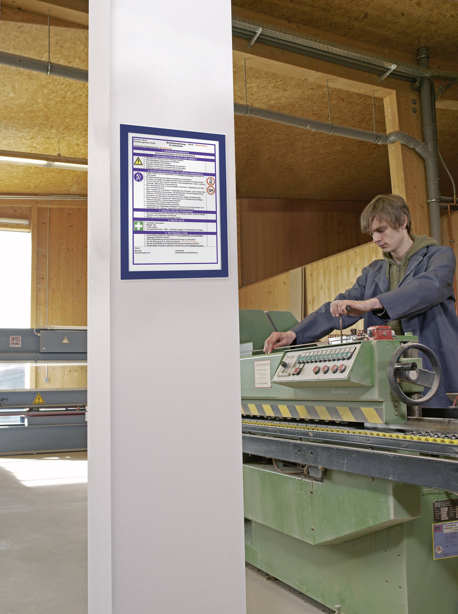 Eine Person bedient eine grüne Holzverarbeitungsmaschine in einer Werkstatt. Sicherheitsanweisungen hängen an einem Pfeiler.