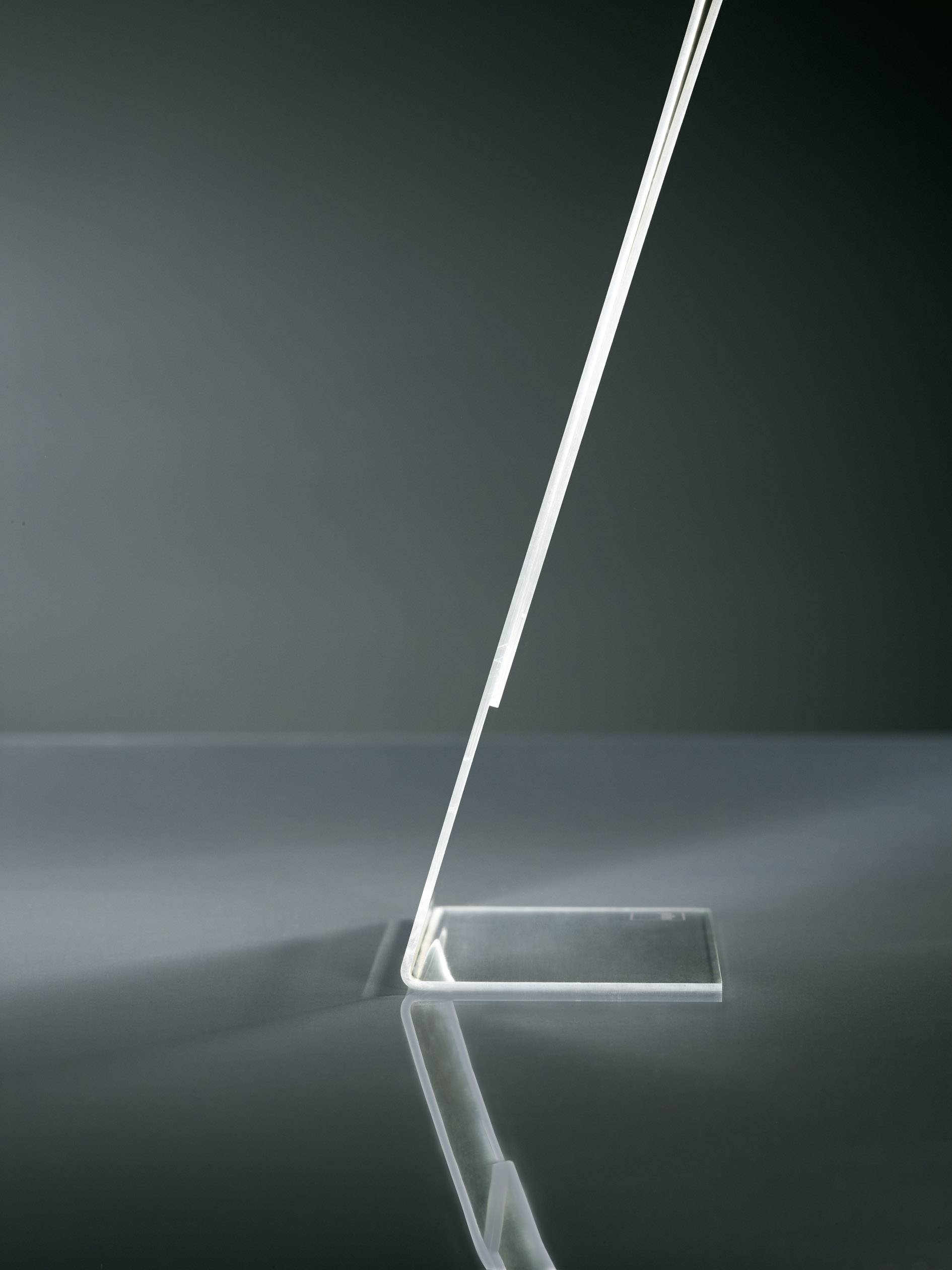Eine moderne, schlanke Tischlampe mit schrägem, minimalistischem Design auf einer glatten, reflektierenden Oberfläche.