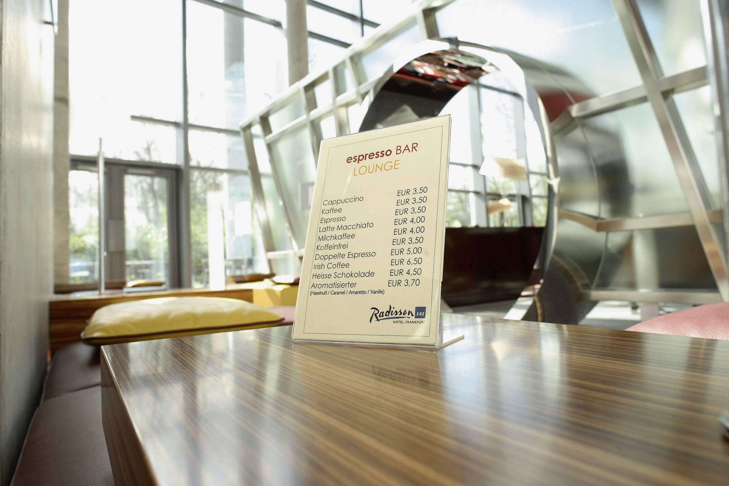 Speisekarte in einem Café zeigt Preise für verschiedene Kaffeesorten, darunter Cappuccino und Latte Macchiato, zwischen 3,50 EUR und 4,30 EUR.