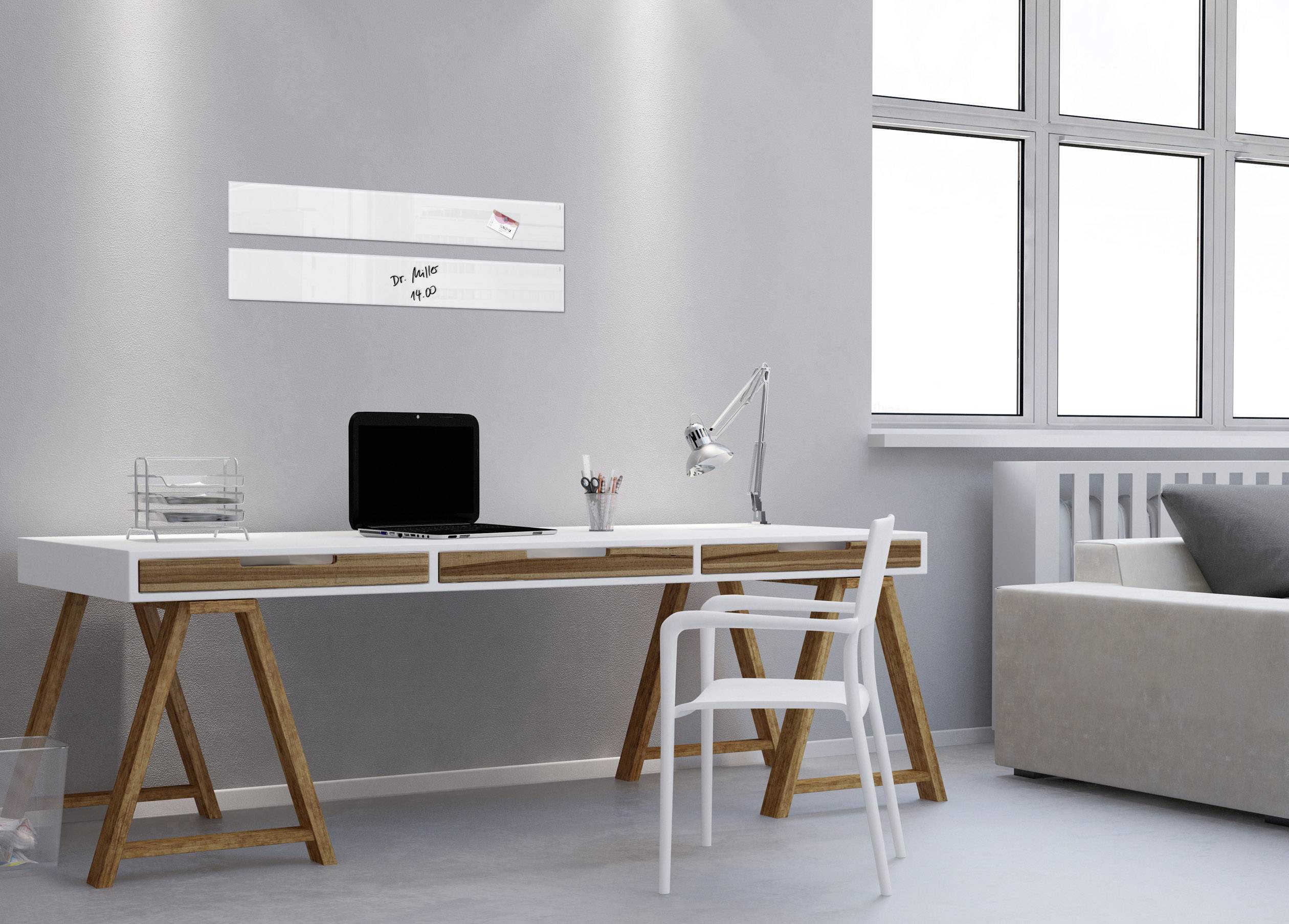 Moderner Schreibtisch mit Laptop und Lampe in hellem Raum. Neben dem Tisch steht ein weißer Stuhl; Fenster auf der rechten Seite.