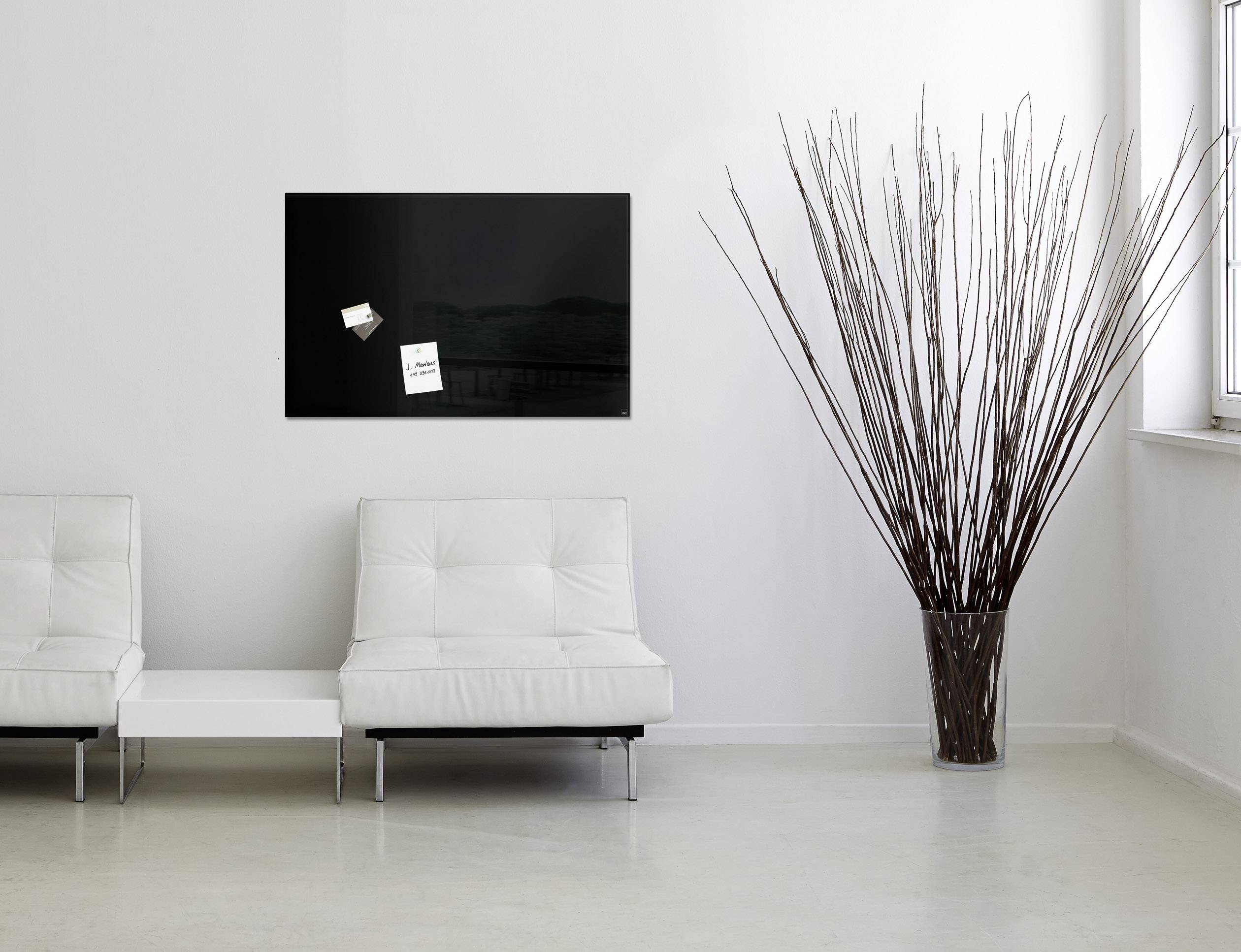 Zwei weiße Sofas in einem modernen, minimalistischen Raum. An der Wand befindet sich eine schwarze Tafel mit kleinen Zetteln.