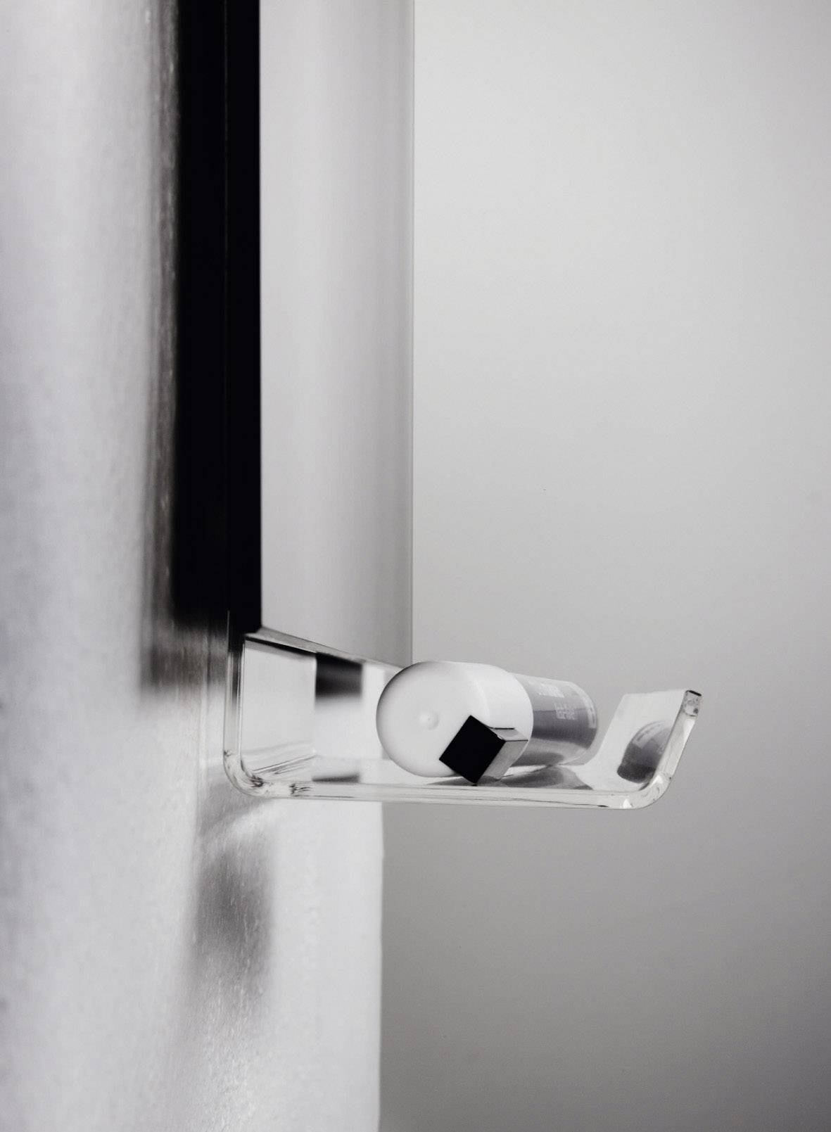 Ein minimalistisches Regal an der Wand hält einen kleinen, runden, weißen Behälter neben einem kleinen, schwarzen Würfel.