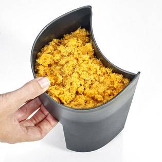 Eine Hand hält einen Metallbehälter, der mit gehackten, leuchtend orangefarbenen Zutaten gefüllt ist.