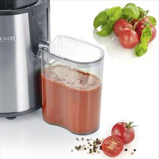 Ein Entsafter gefüllt mit Tomatensaft steht neben frischen Tomaten und Basilikum auf einer weißen Oberfläche.