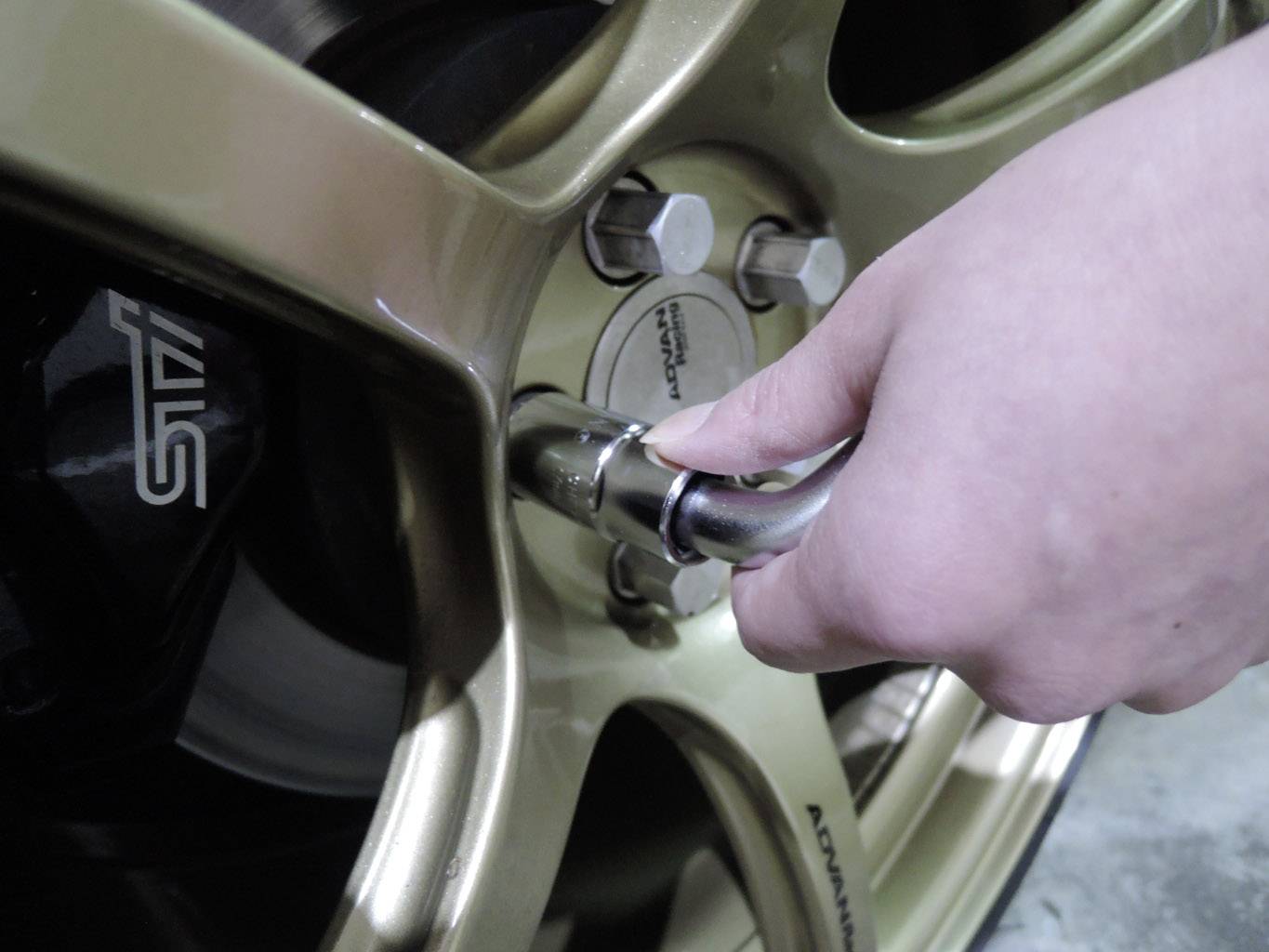 Nahaufnahme einer Hand, die mit einem Schraubenschlüssel eine Radmutter an einer goldfarbenen Felge eines Autos festzieht. Seitenansicht.