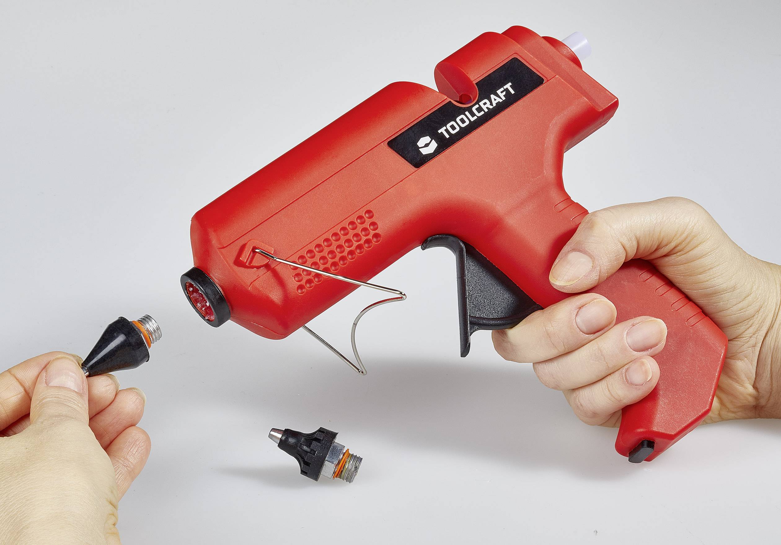 Eine Hand hält eine rote Heißklebepistole, während eine andere Hand eine Düse wechselt.