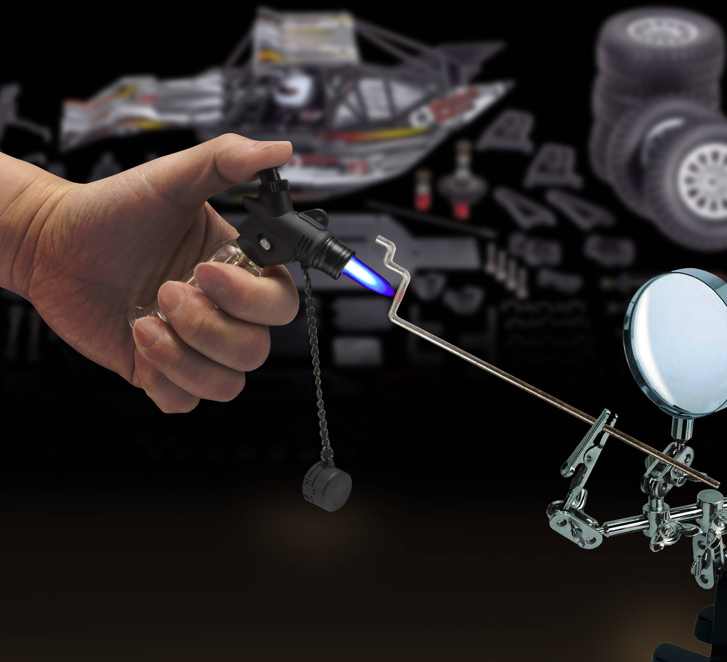 Eine Hand hält einen kleinen Gasbrenner, der eine bläuliche Flamme erzeugt. Daneben steht eine Metallfigur mit einem Schild und Speer.