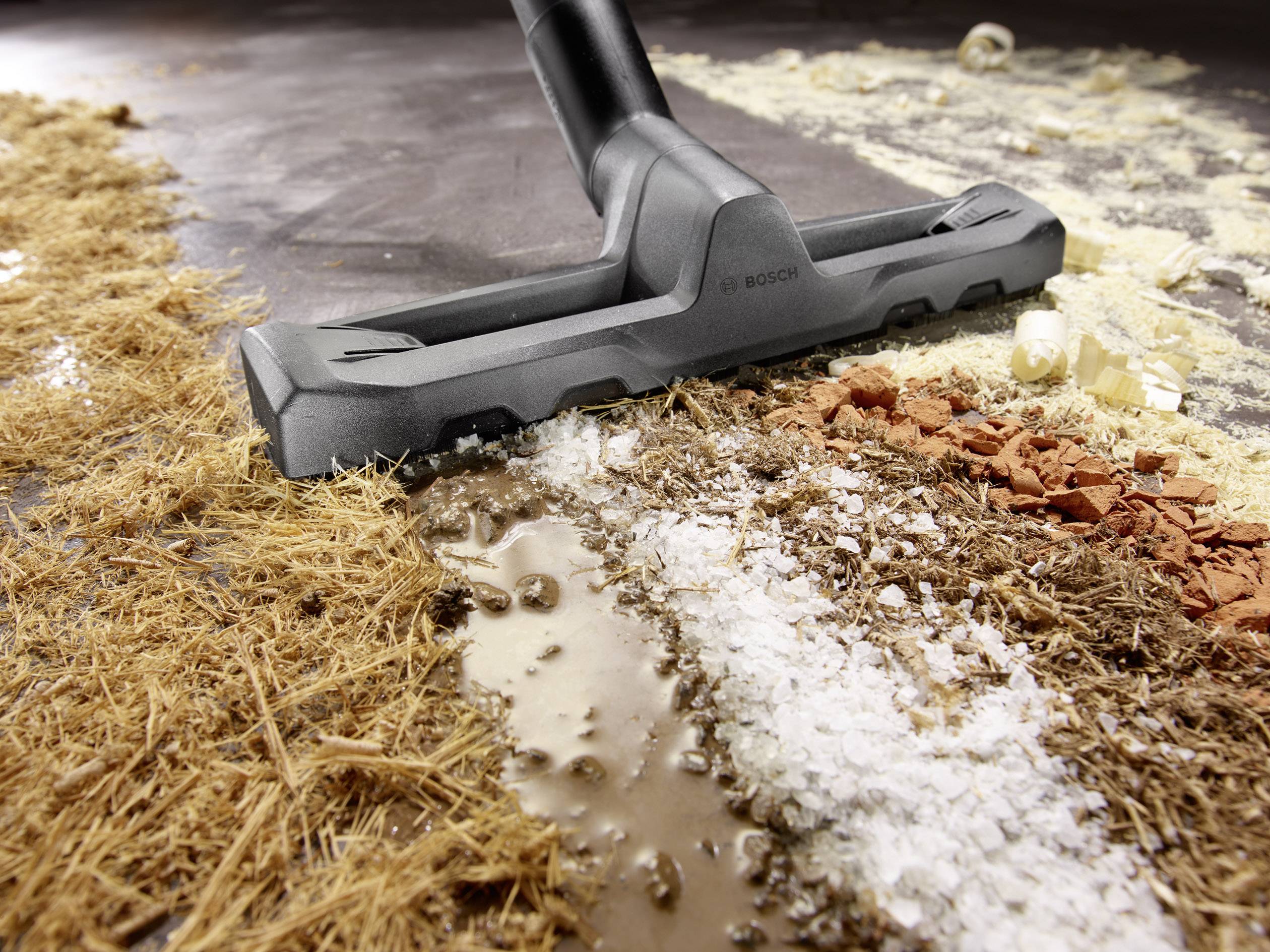 Ein Staubsauger saugt eine Mischung aus Schmutz und verschiedenen Partikeln auf einem Boden.