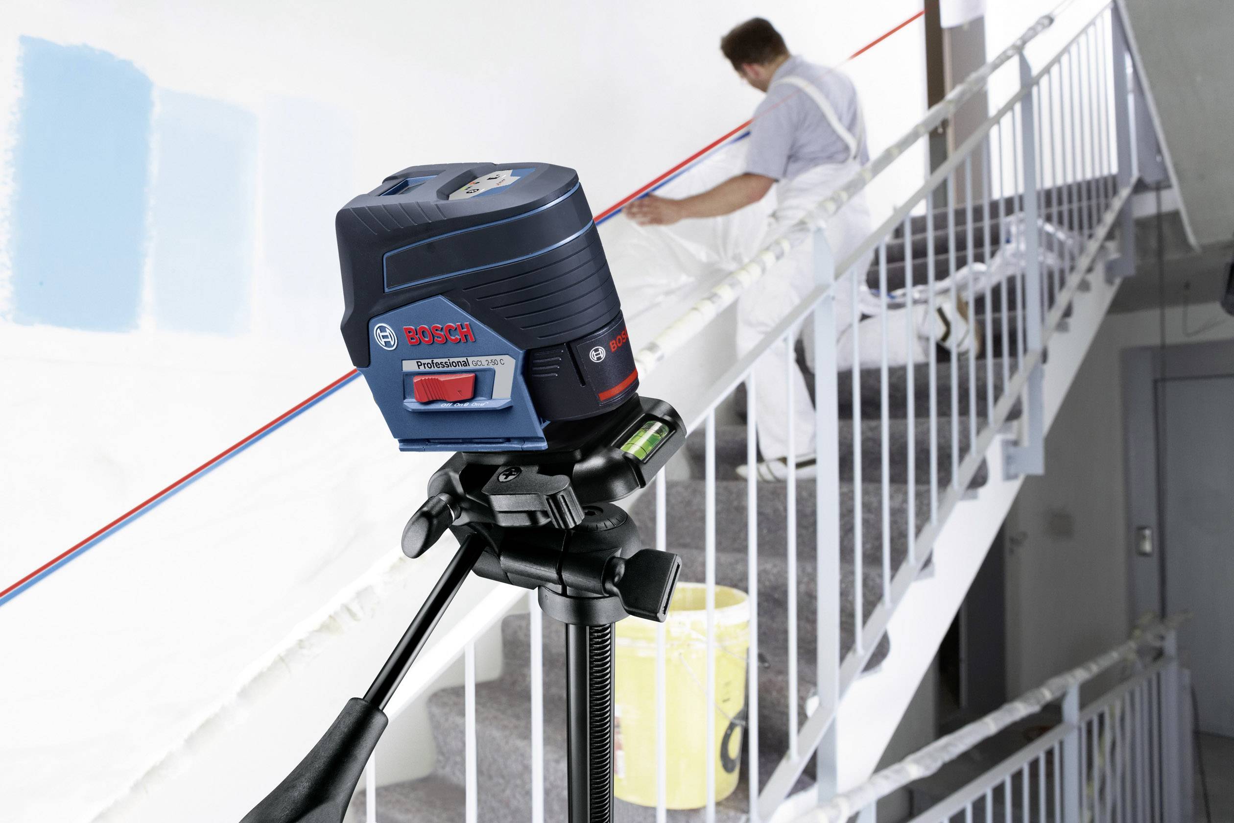 Ein Handwerker arbeitet auf einer Treppe, benutzt ein Lasernivelliergerät auf einem Stativ, um eine rote Linie an der Wand zu projizieren.