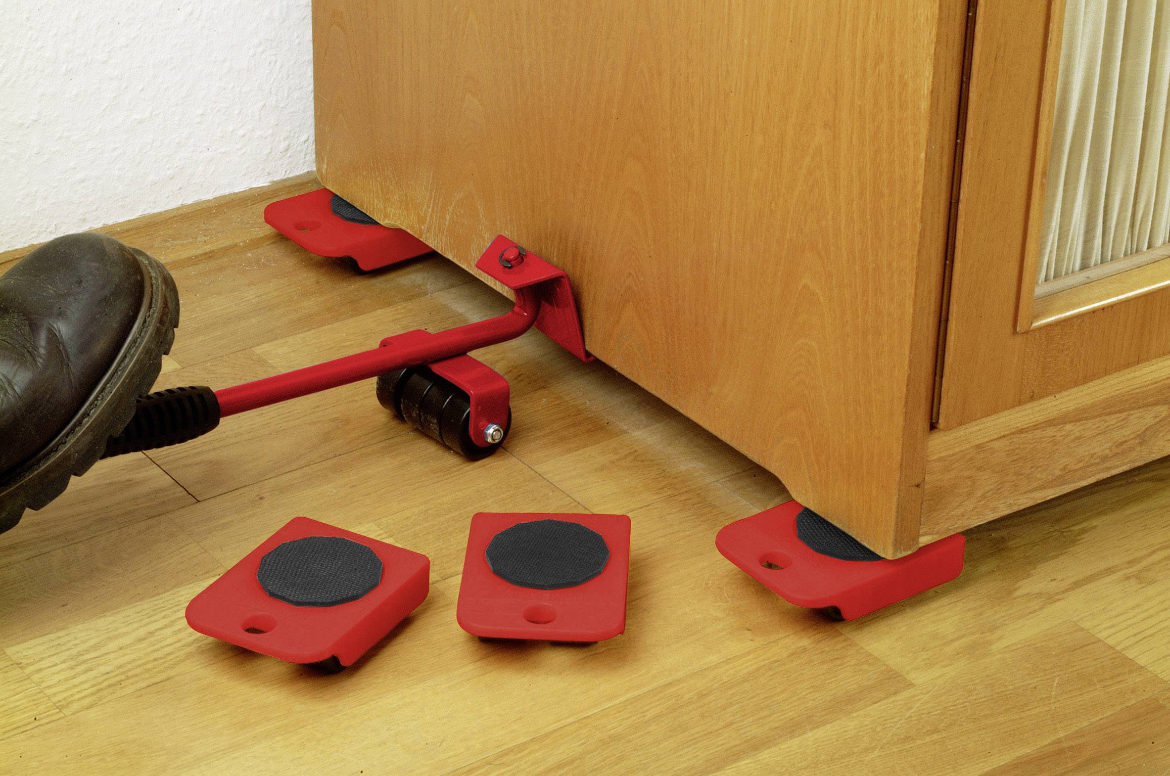 Ein rotes Hebelwerkzeug wird benutzt, um ein Möbelstück anzuheben. Rote Möbelverschieber werden darunter platziert.