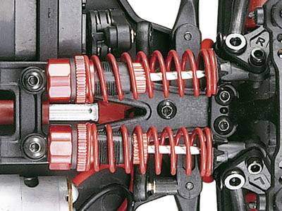 Nahaufnahme einer roten, doppelten Federung eines RC-Autos, montiert an der Vorderachse, zeigt komplexe mechanische Komponenten.